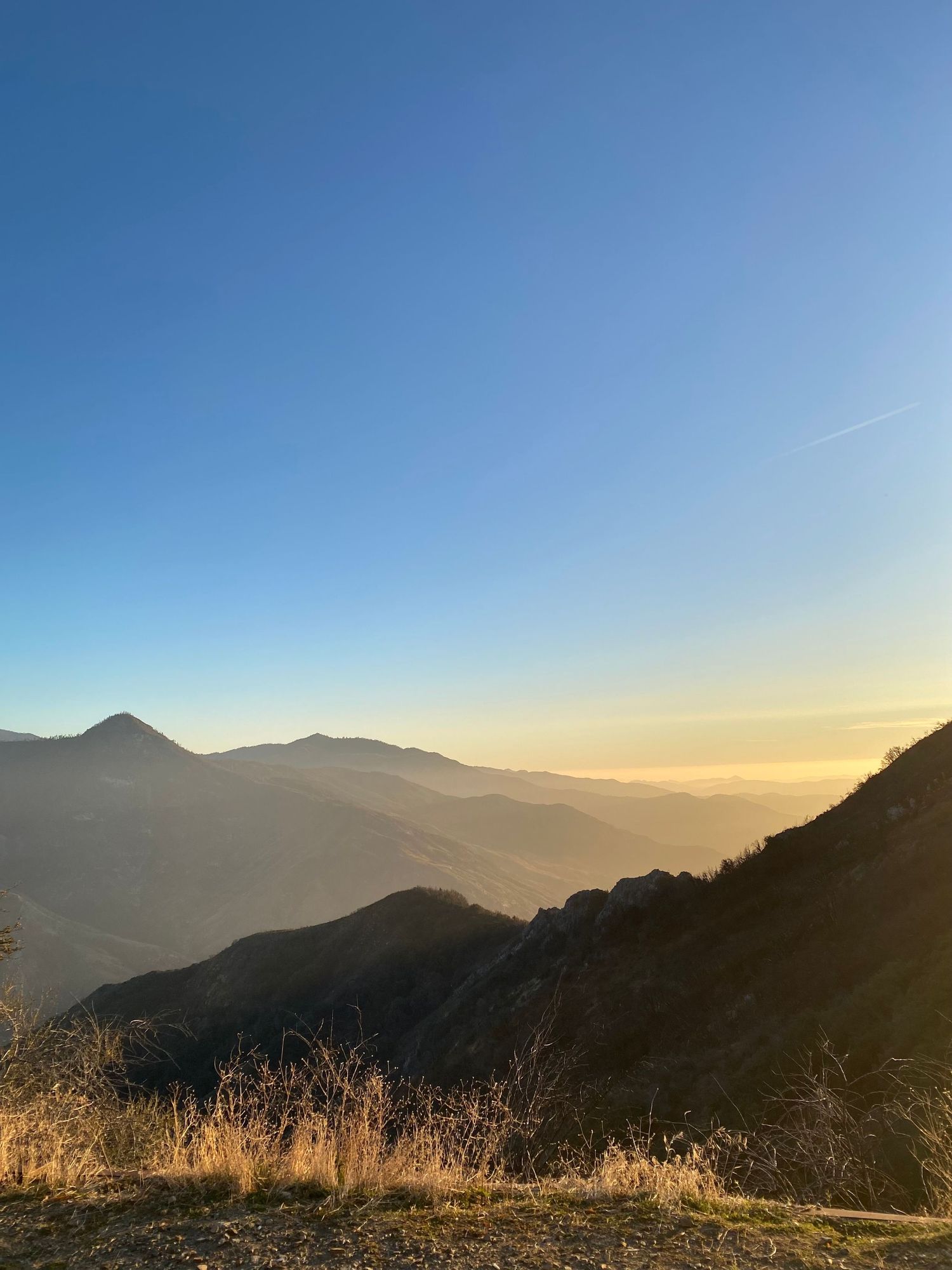 Golden sunset light illuminates mountain ranges and valleys under clear blue sky in scenic wilderness landscape.
