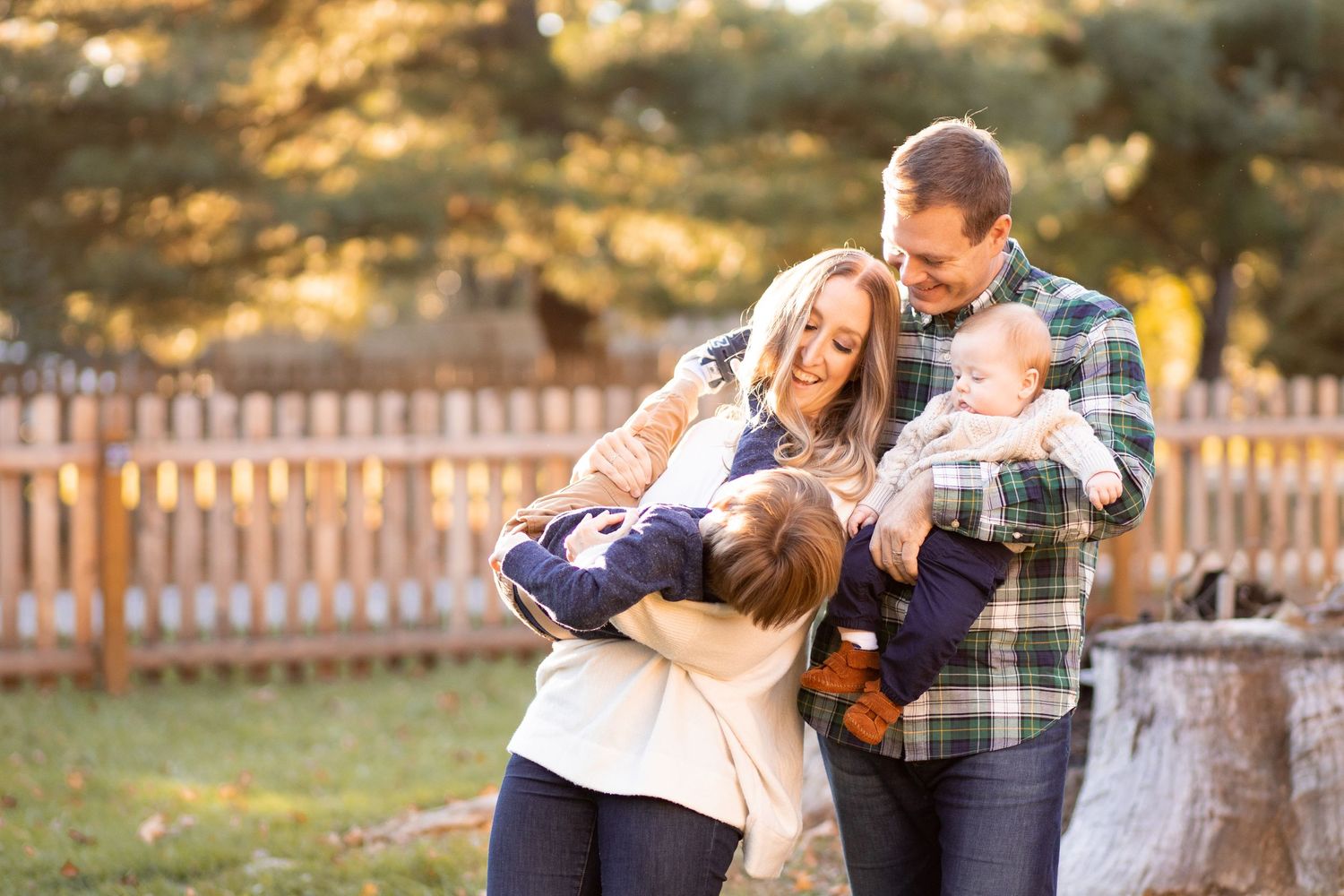 A loving family shares joyful laughter together in a backyard during golden hour with a wooden fence in the background.