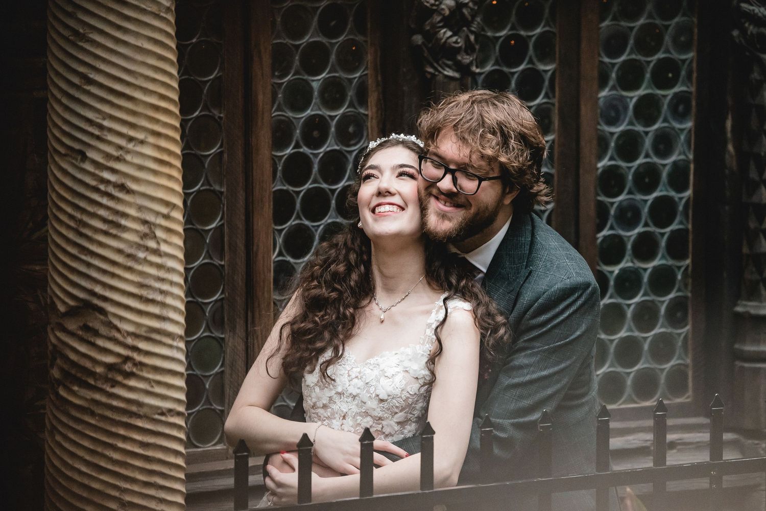 A joyful couple in wedding attire share a candid moment by a vintage stained glass window.