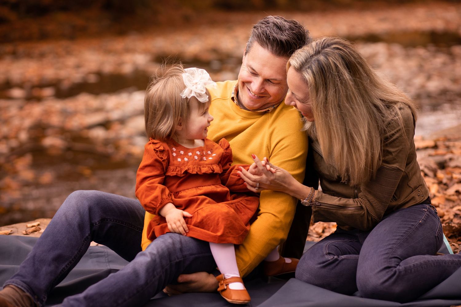 A couple in autumn attire shares tender moments on fallen leaves in a romantic outdoor photoshoot.
