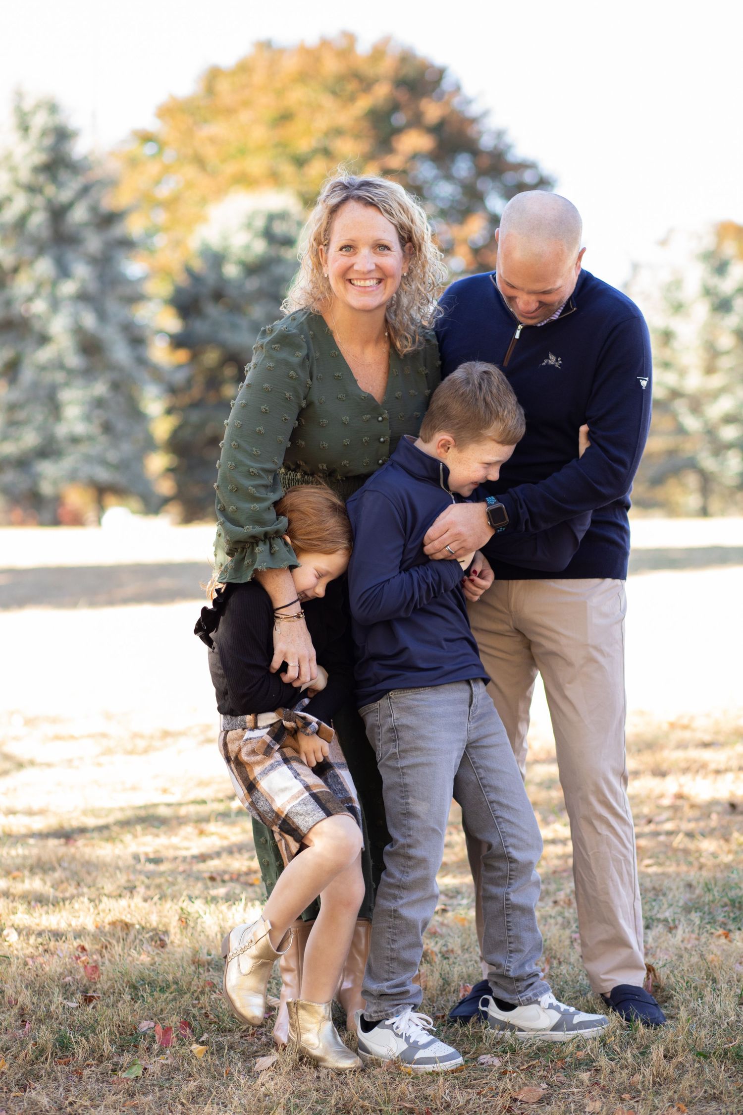 A family shares a joyful moment together outdoors on an autumn day with fall foliage in the background.