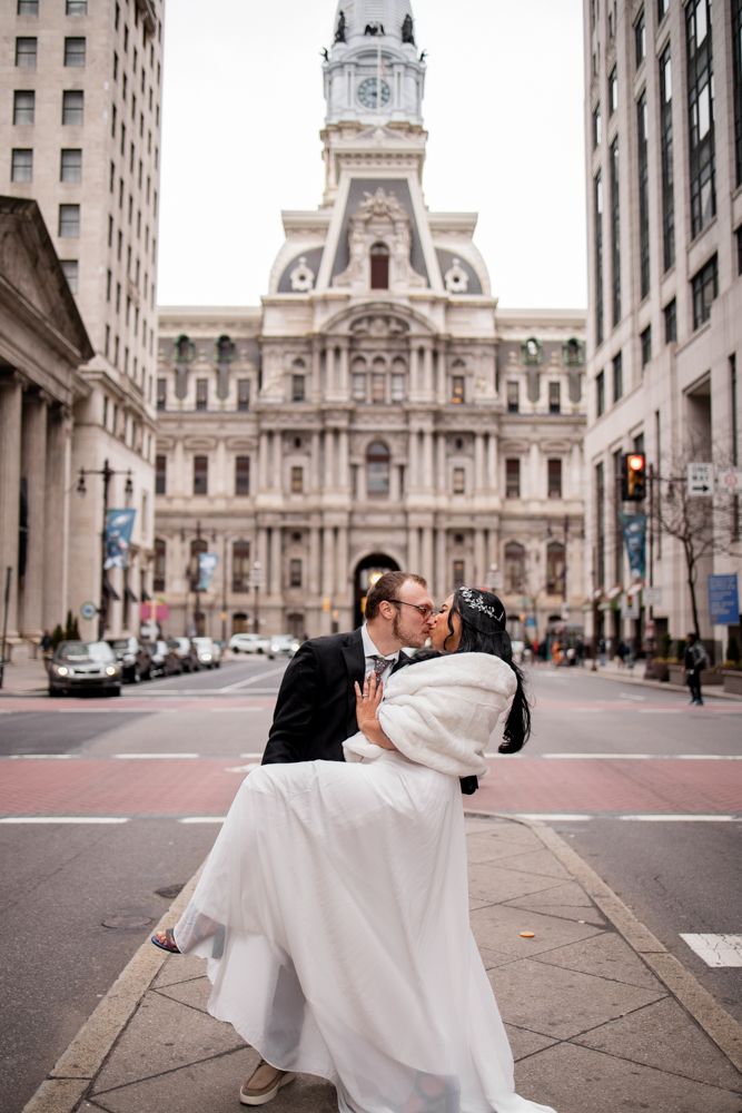 A couple share a romantic dip kiss in front of Philadelphia City Hall during their wedding photoshoot.