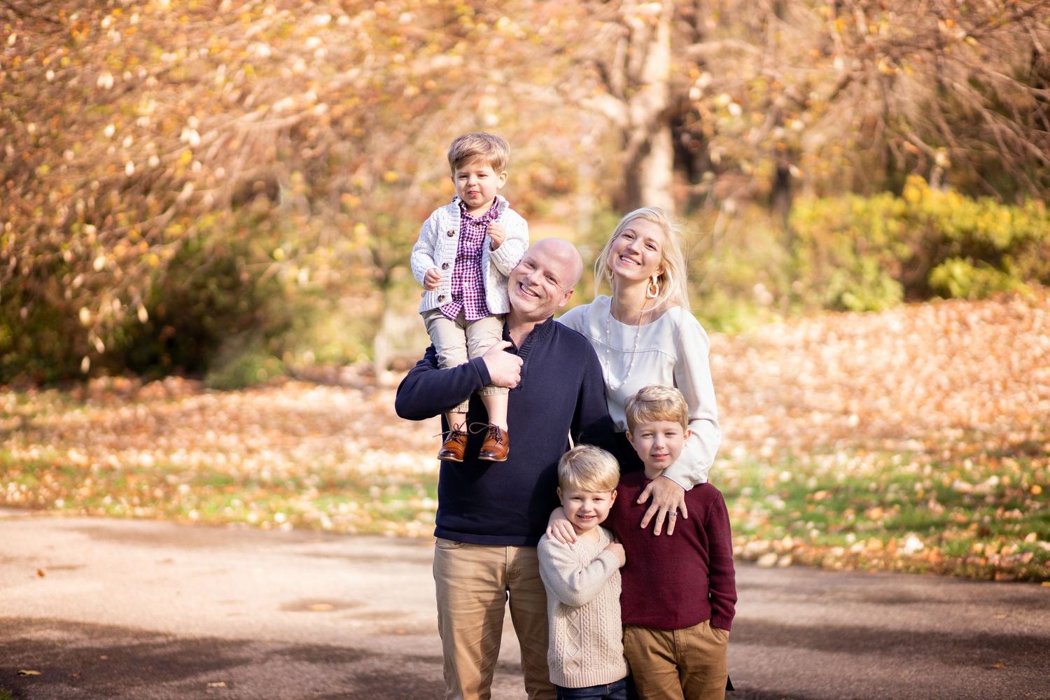 A family enjoying a stroll together on an autumn path with fallen leaves and golden foliage in the background.