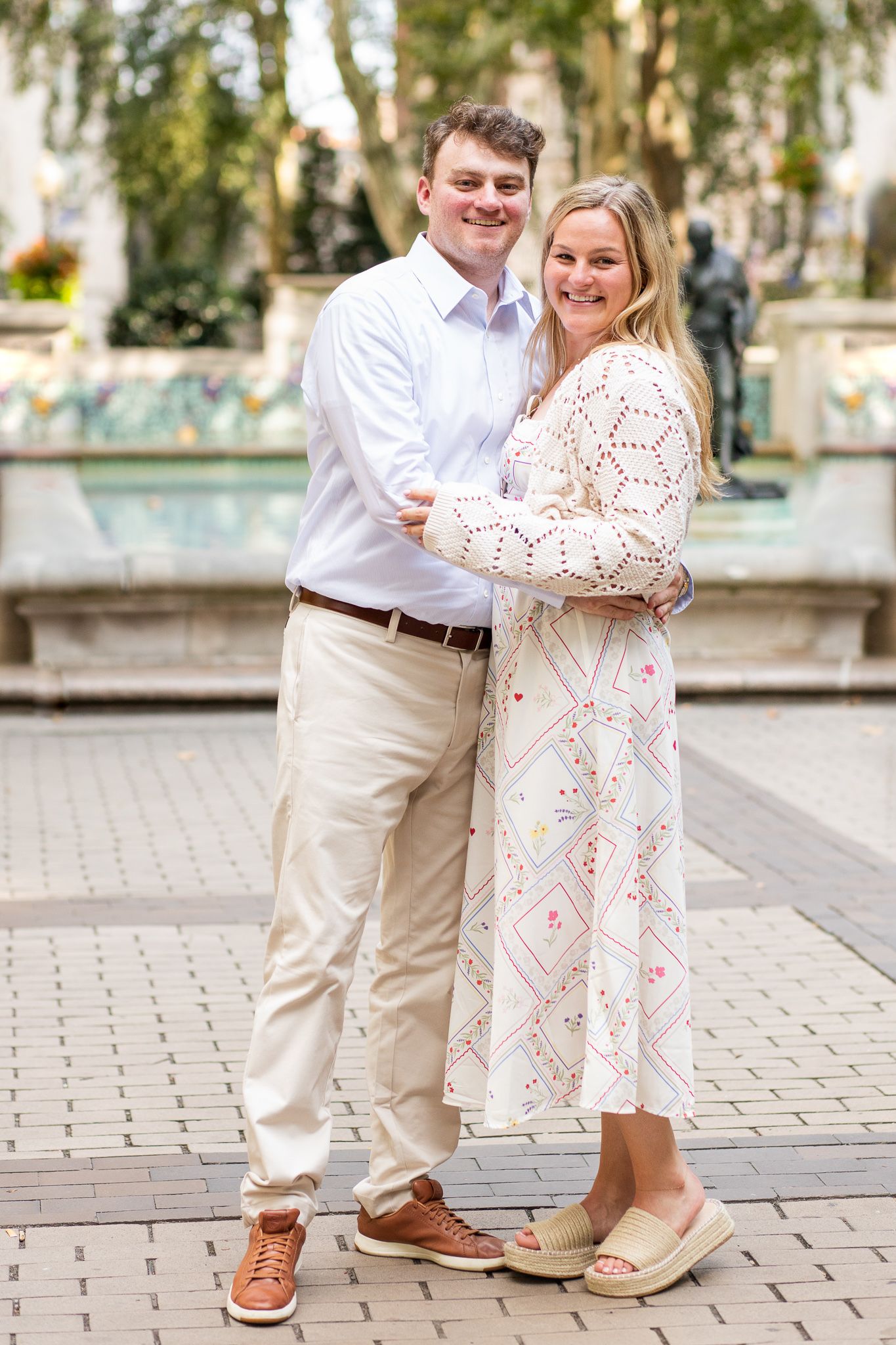A couple in coordinated outfits shares playful moments on a brick paved walkway surrounded by greenery.