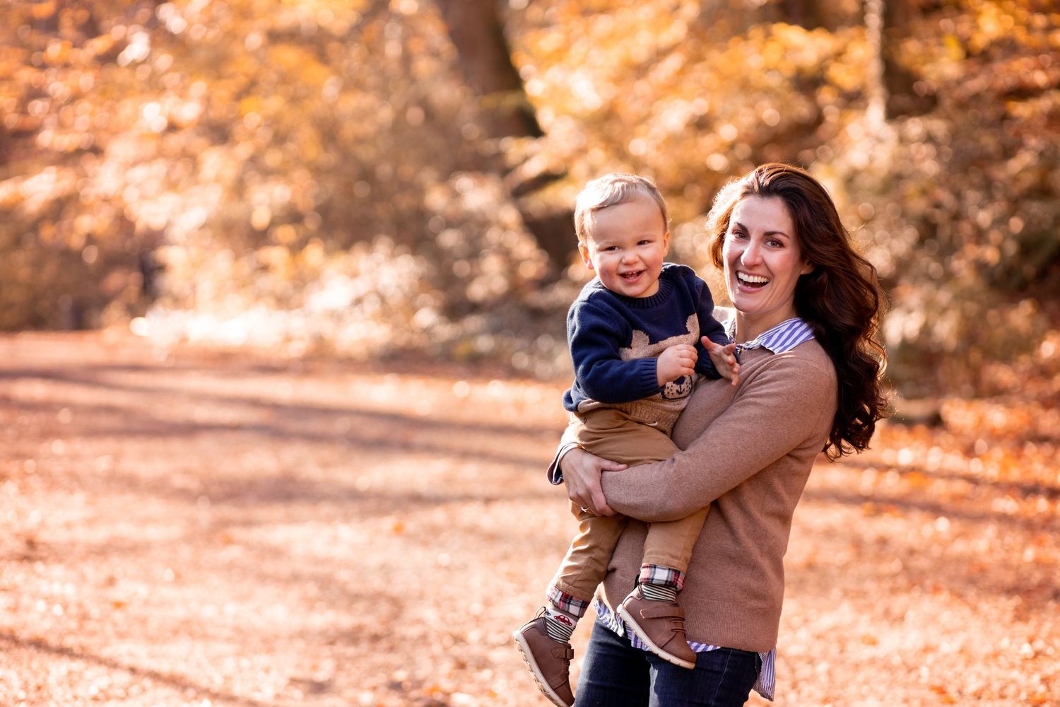 A happy family walks together through an autumn forest with warm golden sunlight filtering through the trees.