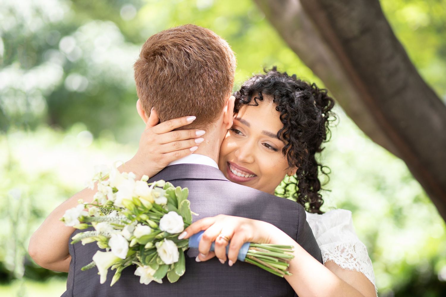Romantic wedding couple sharing intimate moments outdoors surrounded by lush greenery and white floral bouquet.