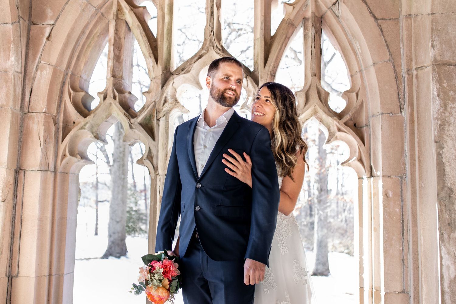 A couple shares a romantic moment in a beautiful stone archway surrounded by snow-covered trees in winter.