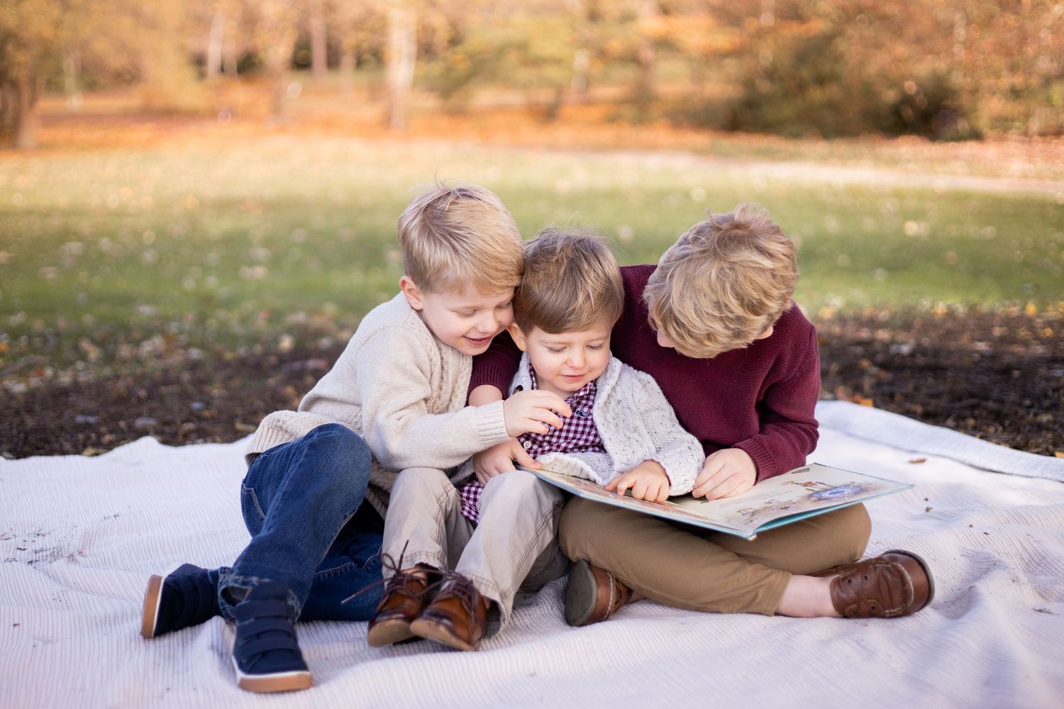 People lying on fall leaves reading books together in an outdoor setting during autumn.