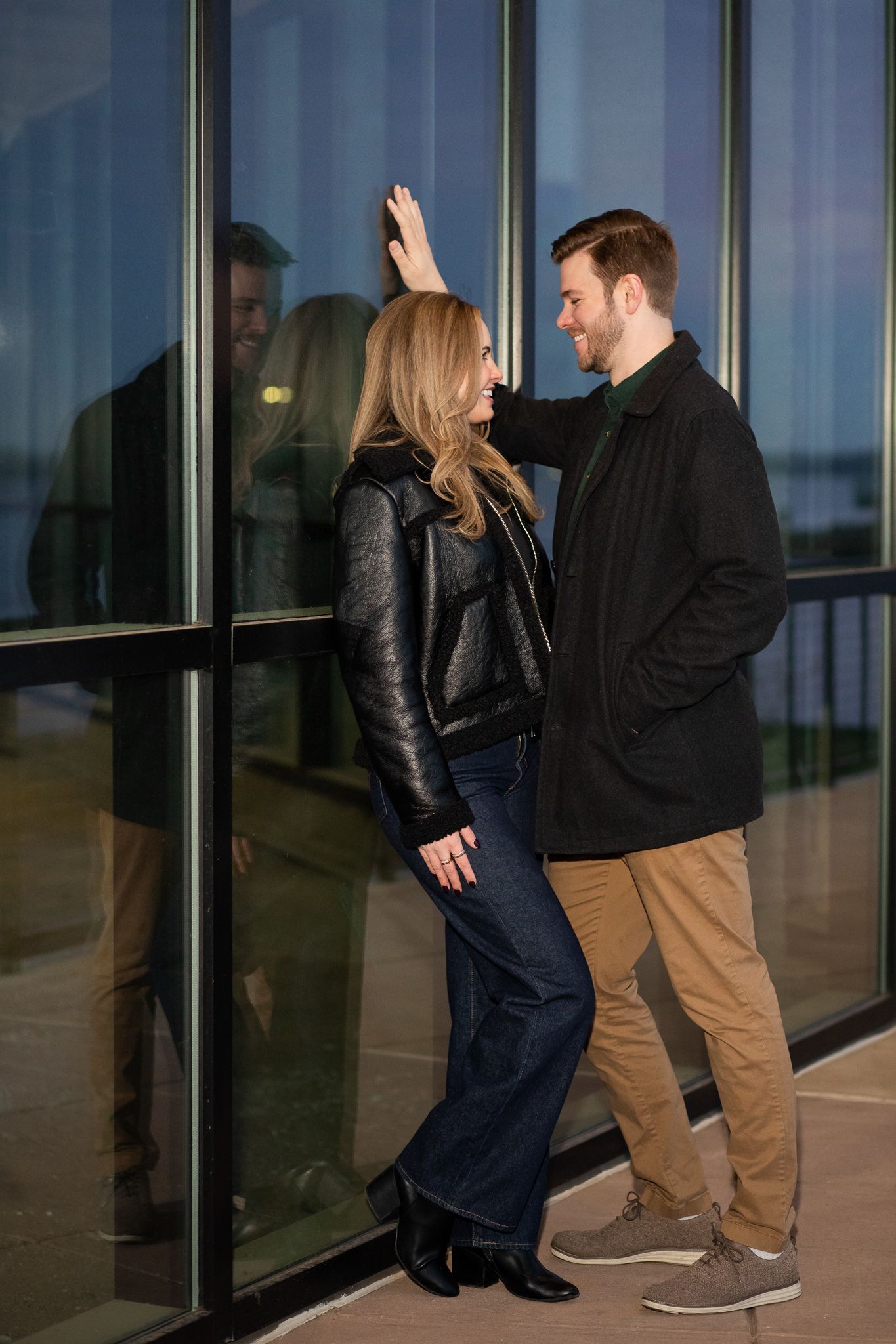 Two people in casual attire walking together and gesturing while passing by glass windows during sunset.