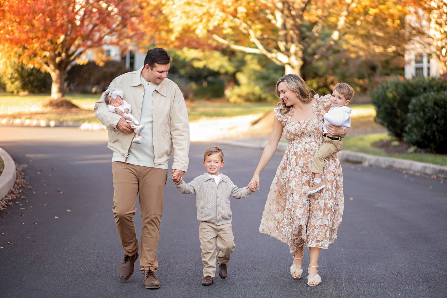 A joyful family walking hand in hand on a paved path during golden autumn sunset with leaves in the background.