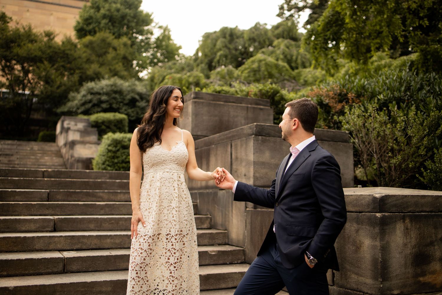 A couple on stone steps during an engagement photoshoot in a garden setting with elegant attire.