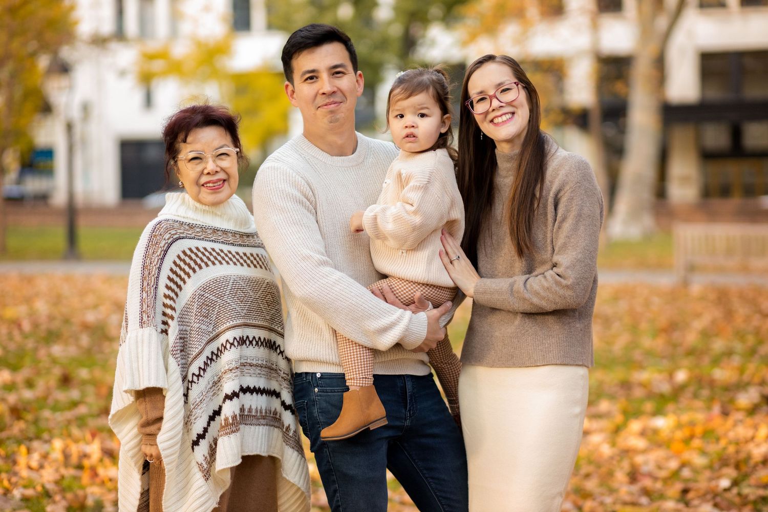 A group of people pose together outdoors on an autumn day with fallen leaves scattered on the ground.