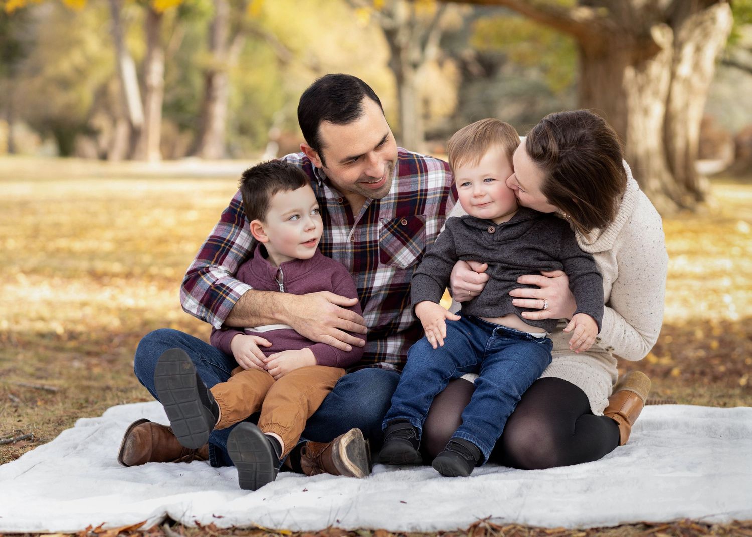 Family rests together on a cozy blanket during fall season photoshoot outdoors.