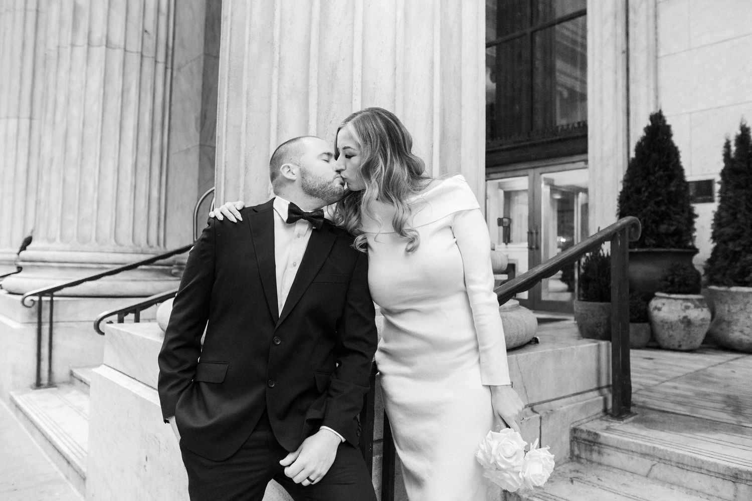 Romantic portrait of a newlywed couple standing outside a classic white stone building with ornate columns.