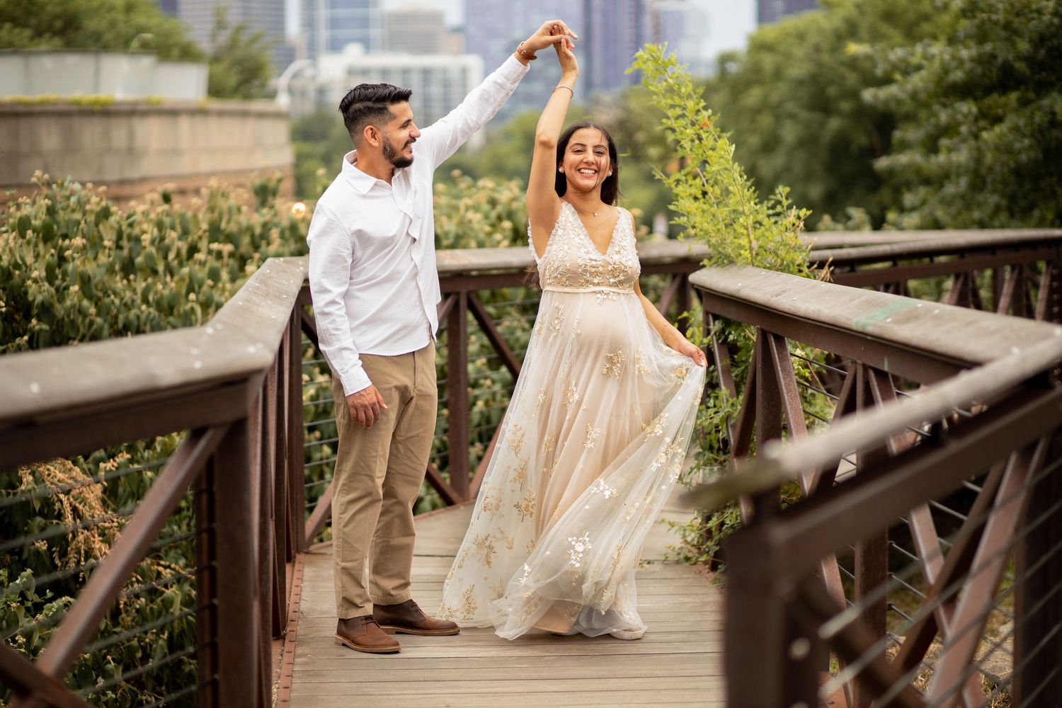 A couple dancing together on a wooden bridge walkway surrounded by greenery in an urban setting.