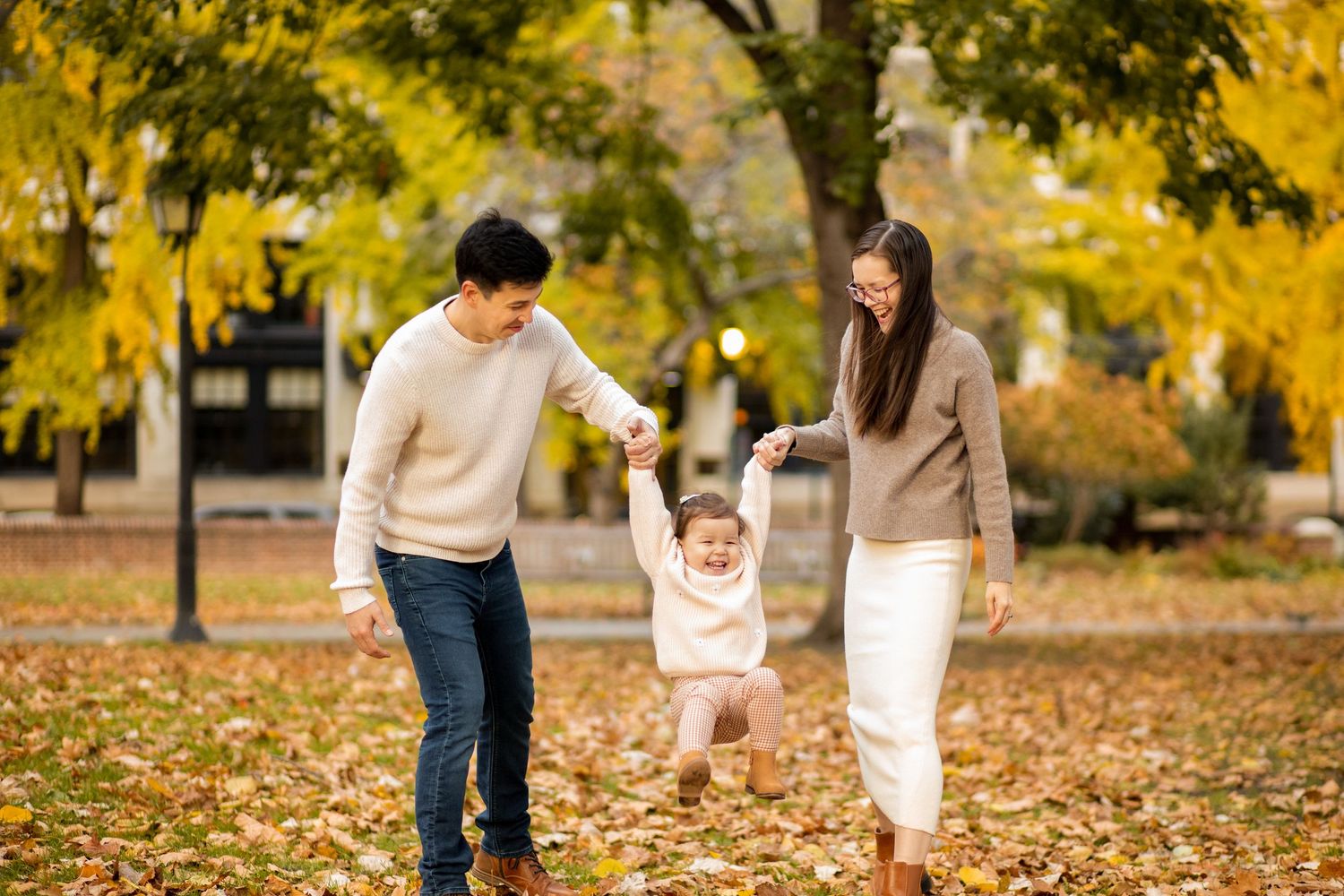 Family walking and playing together in a park on an autumn day with yellow leaves falling from trees.