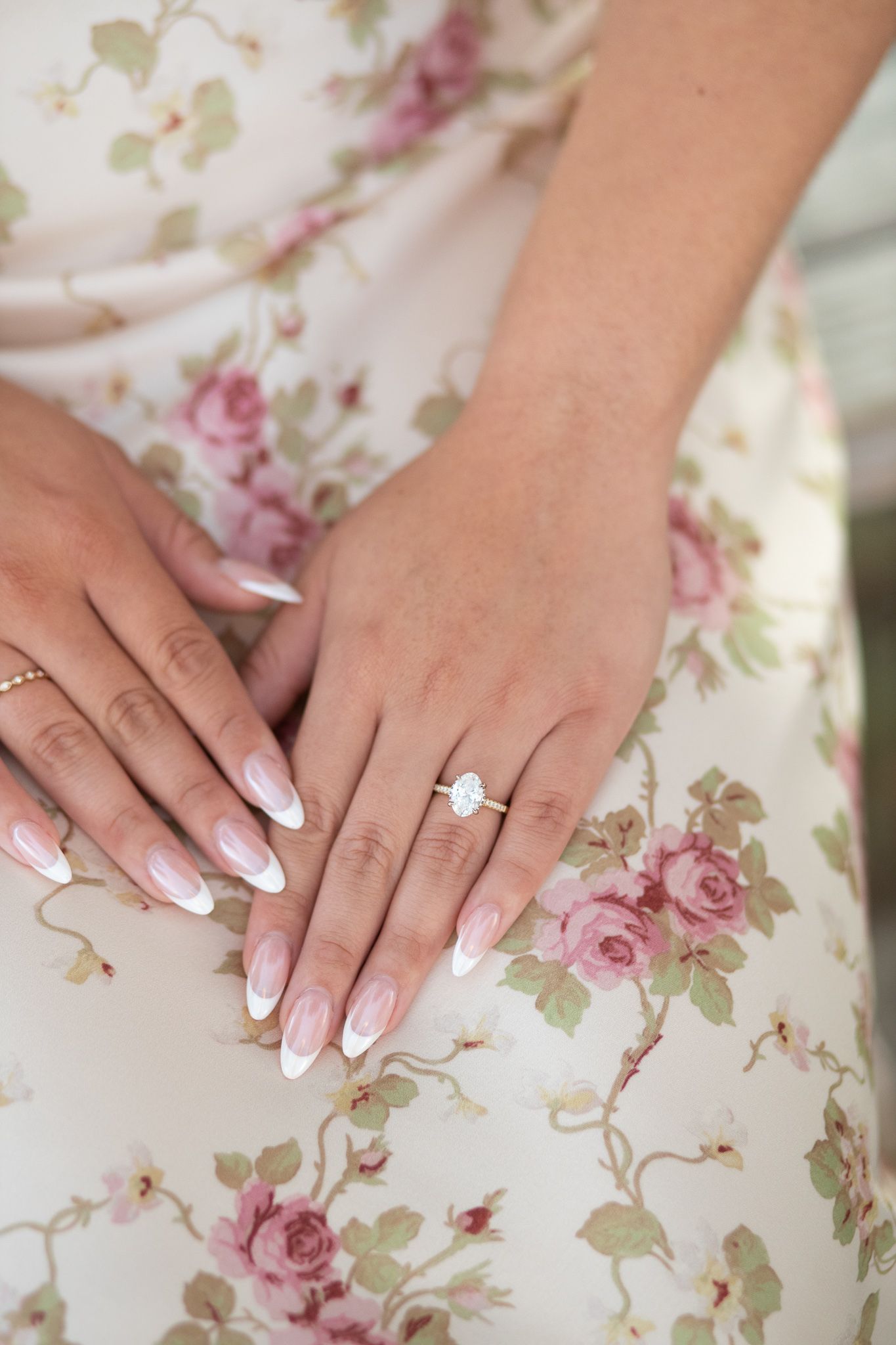 Perfectly manicured french tip nails and engagement ring displayed on floral dress with pink roses pattern.