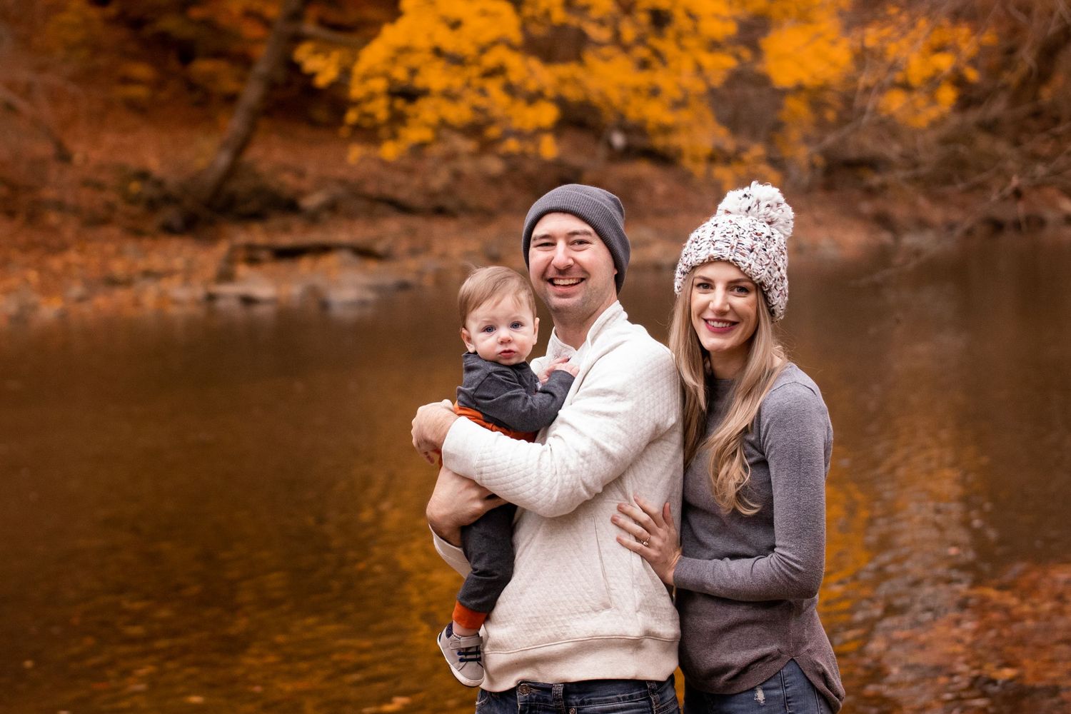 People enjoying a warm autumn day by a lake surrounded by vibrant orange foliage and fallen leaves.