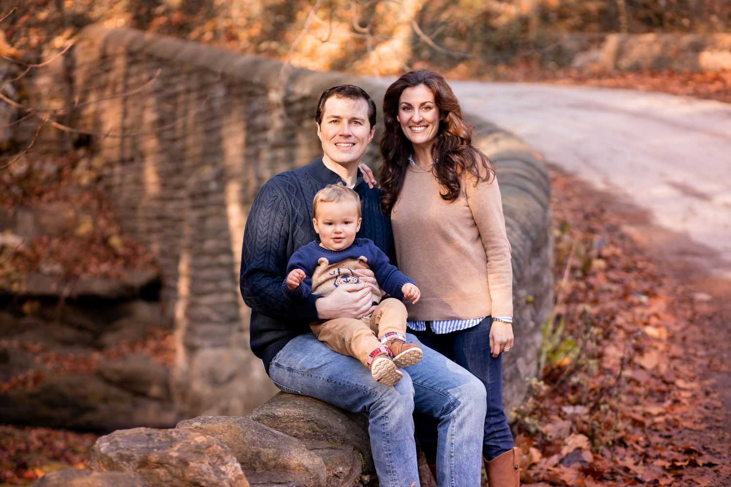 Family sitting together outdoors on rocky path during autumn with fallen leaves and natural scenery.