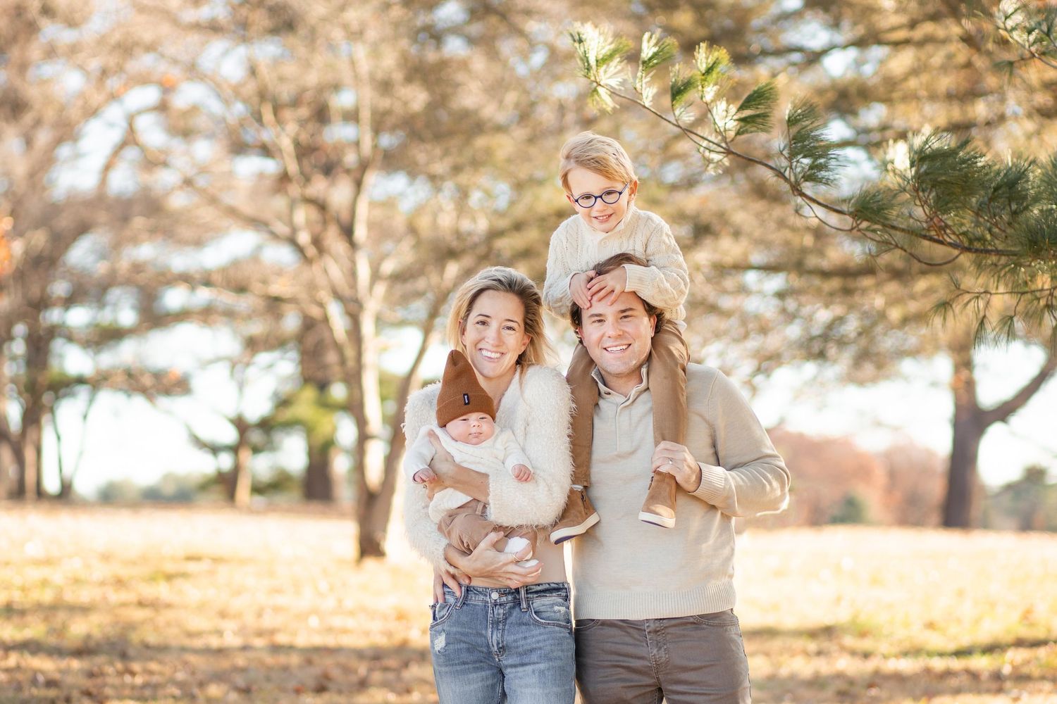 Happy family enjoying a sunny autumn day together in a park with pine trees in the background.