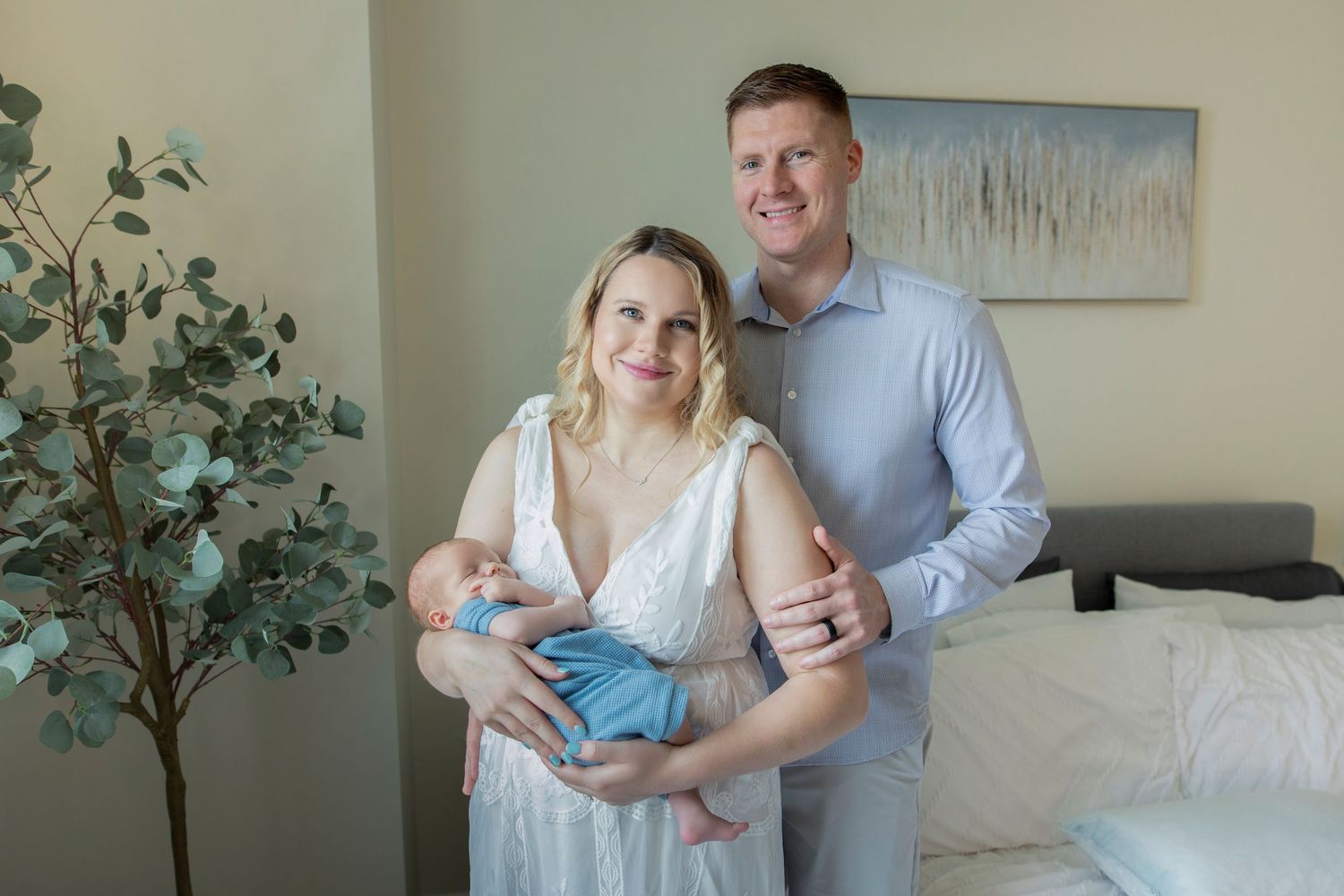 A couple shares tender moments together in a light-filled room with a baby and decorative plants.