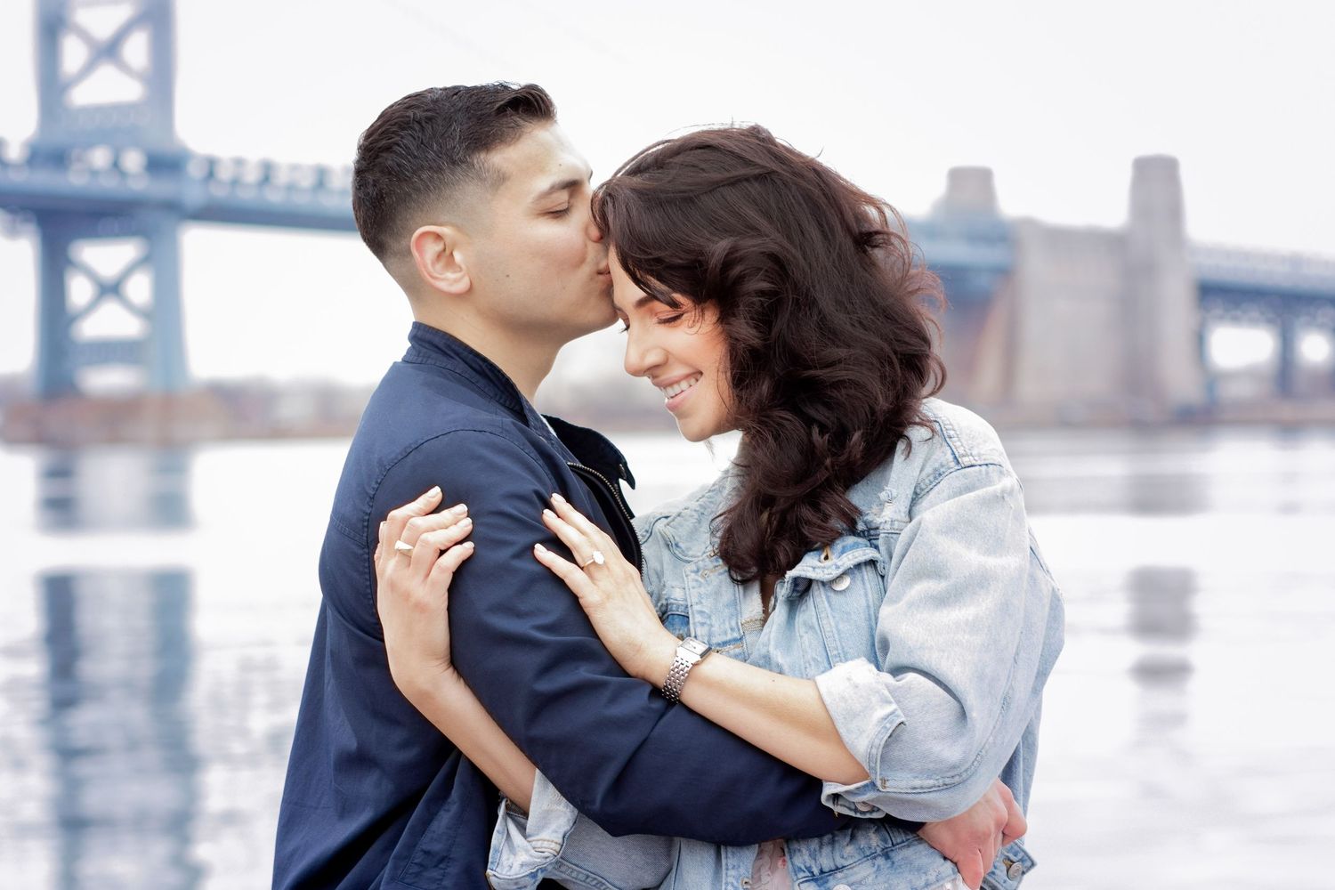 A romantic couple embraces by a waterfront cityscape during an engagement photoshoot session.