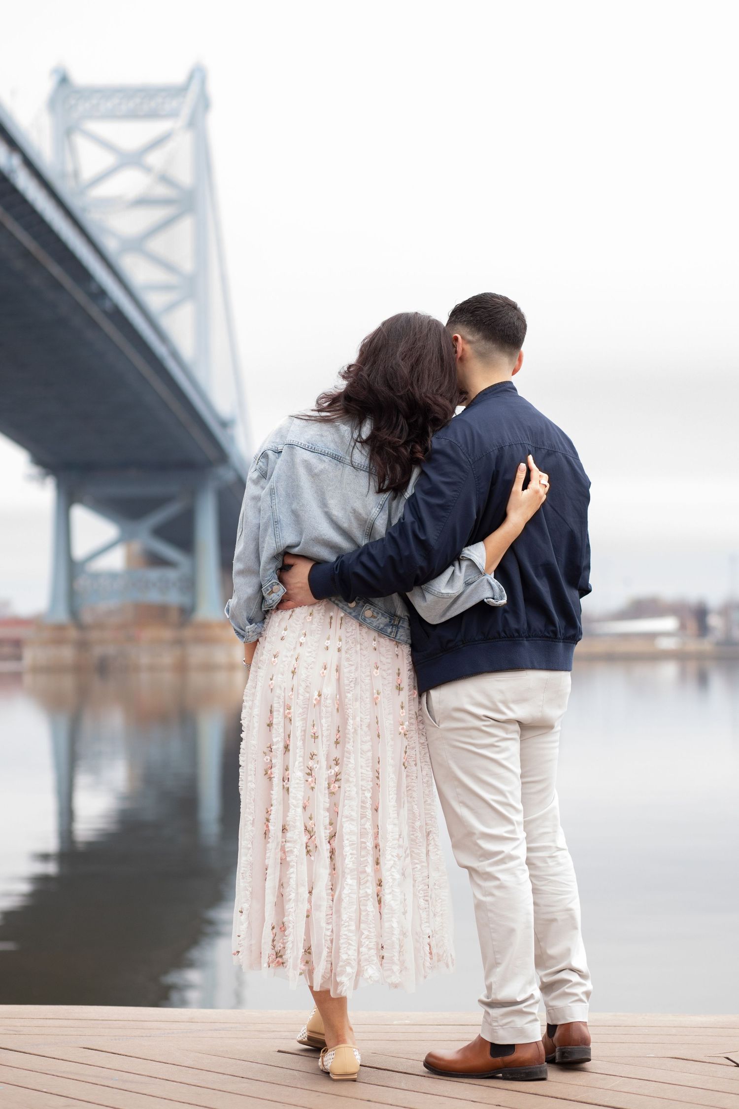 A romantic couple embraces while viewing the Benjamin Franklin Bridge from Penn's Landing pier in Philadelphia.