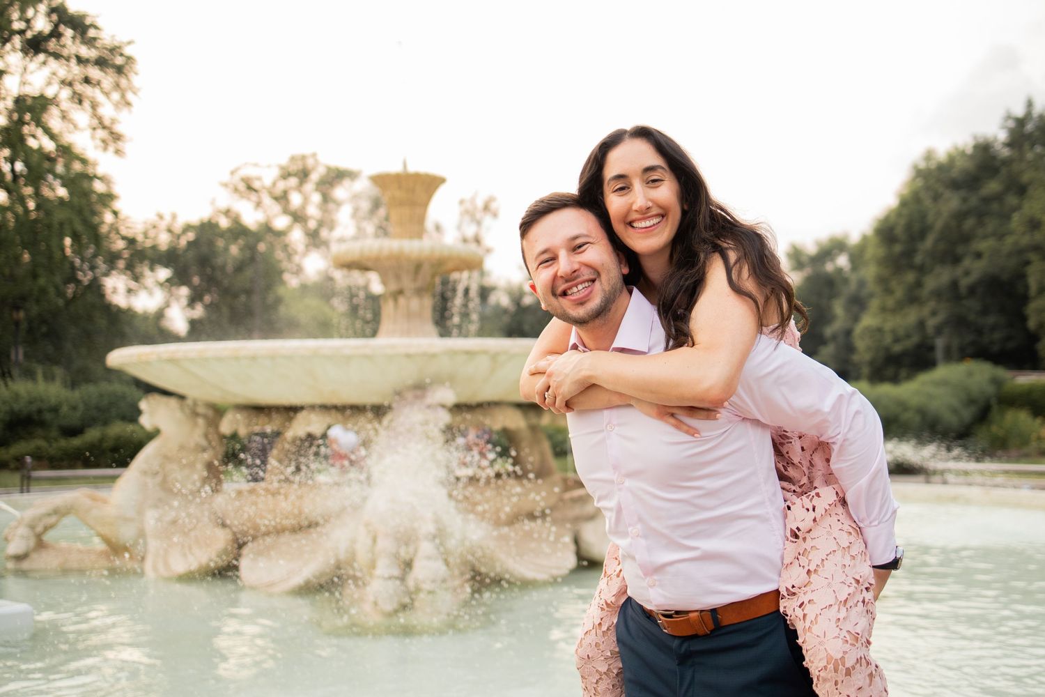 Couple shares joyful moment together by ornate fountain in garden during golden hour sunset.