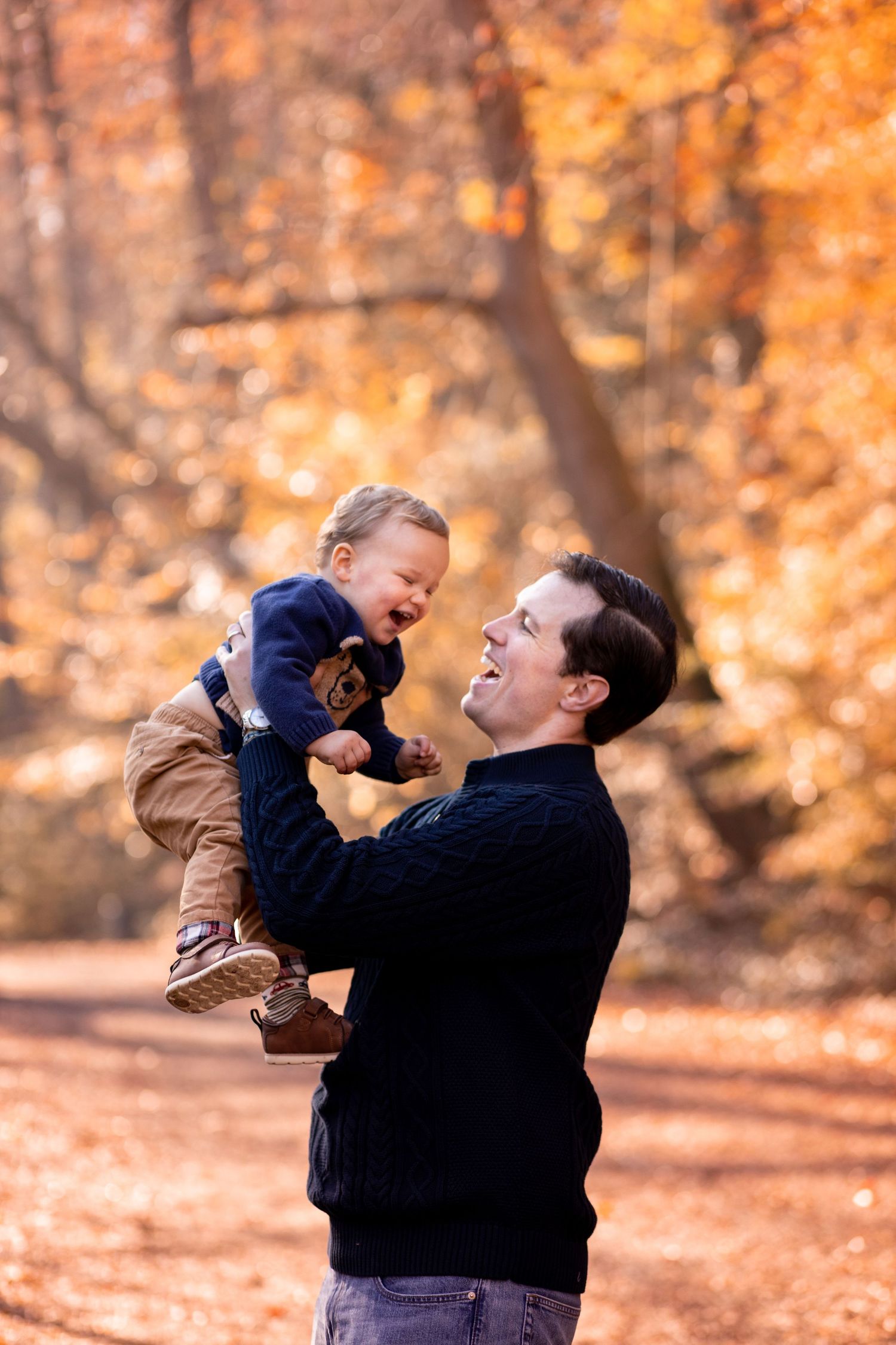 A man lifts a small child while playing outdoors among vibrant fall foliage and autumn colors.
