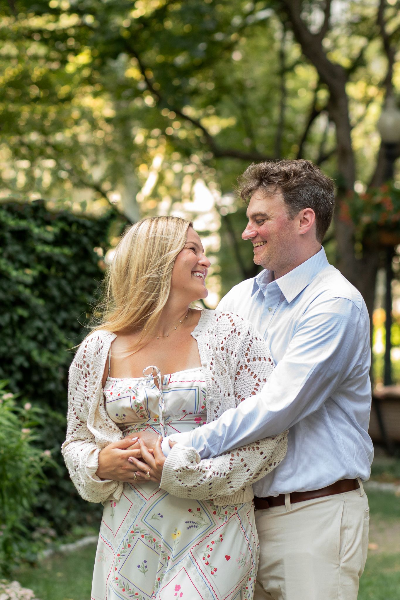 A couple laughs together while embracing in a sunlit garden setting.
