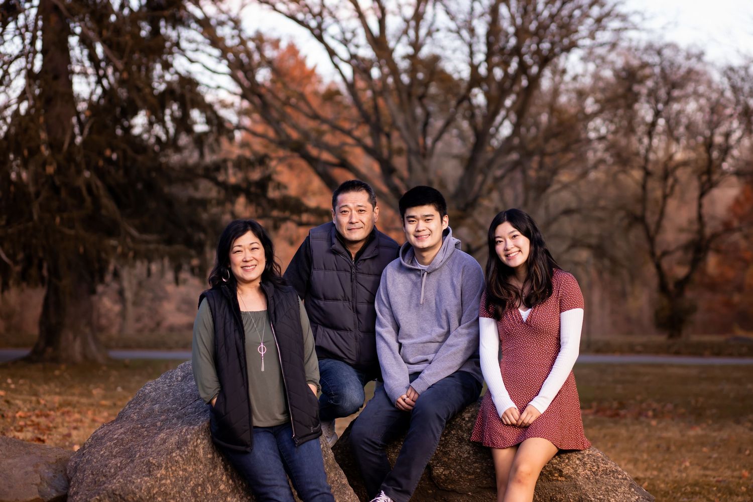 A small group sits together outdoors on a path surrounded by autumn trees during golden hour.