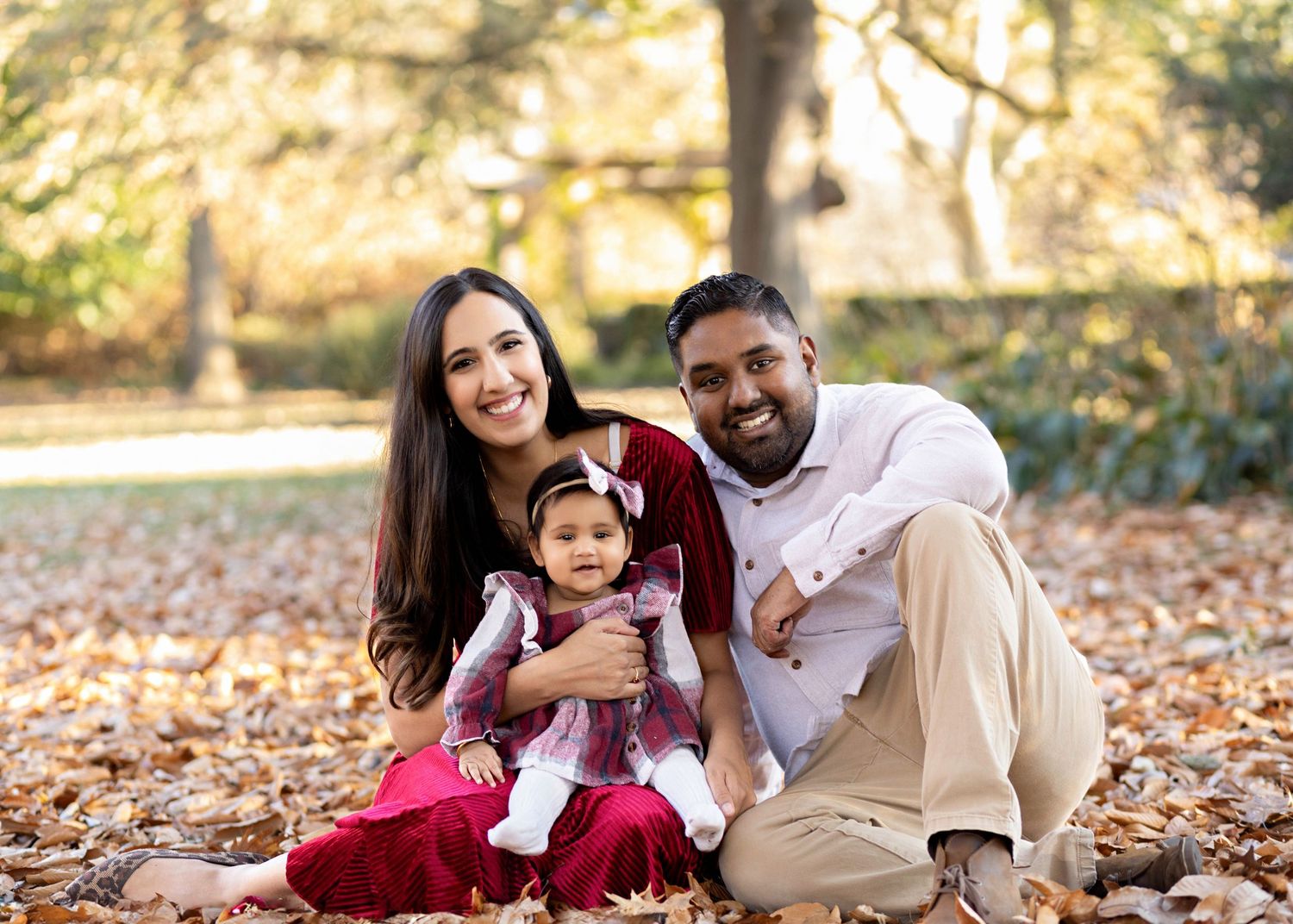 A family sits together on fallen autumn leaves in a park during a warm golden-hour photo session.