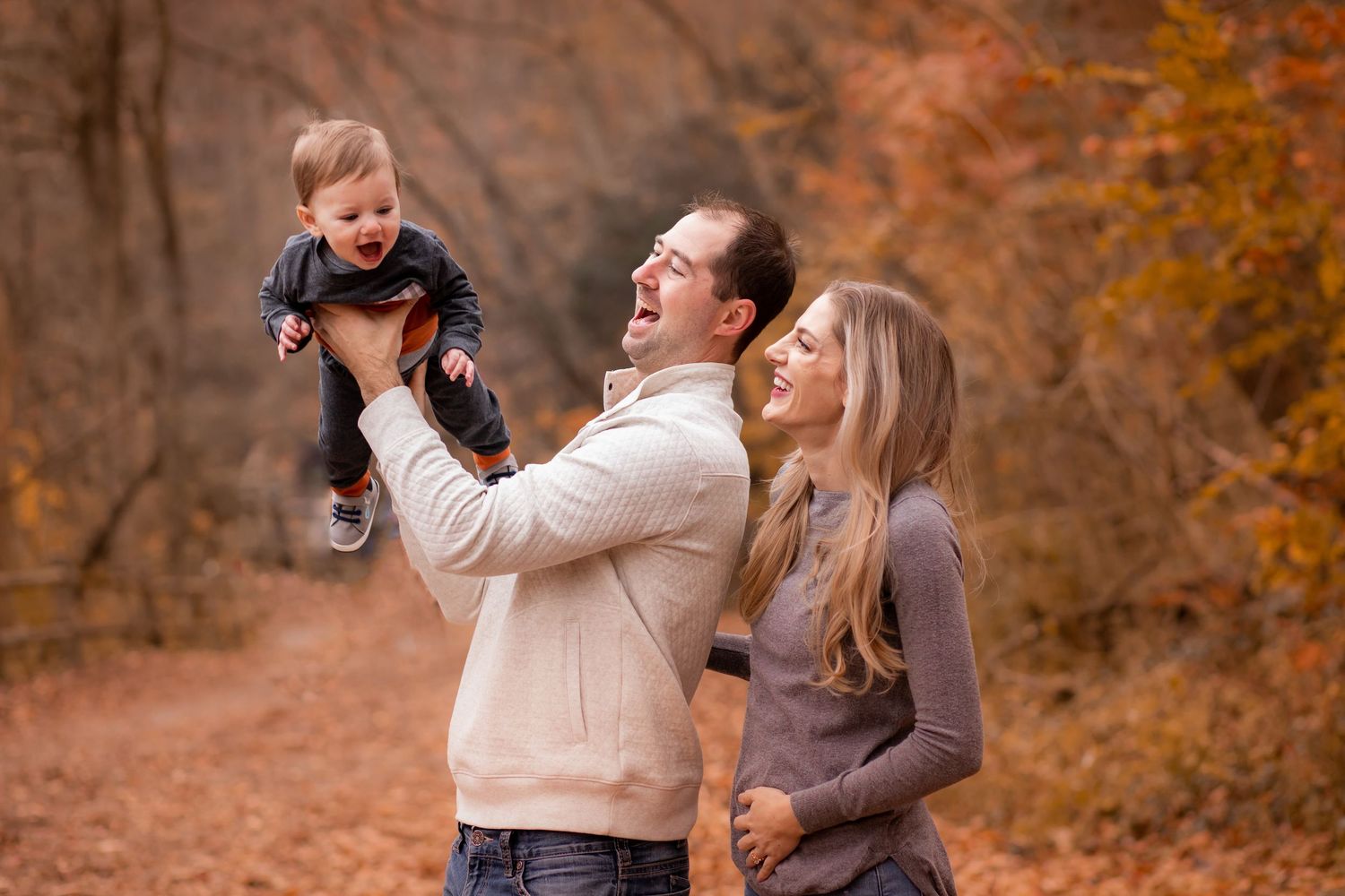 Happy couple enjoying autumn walk with baby in forest with orange fall foliage in background.