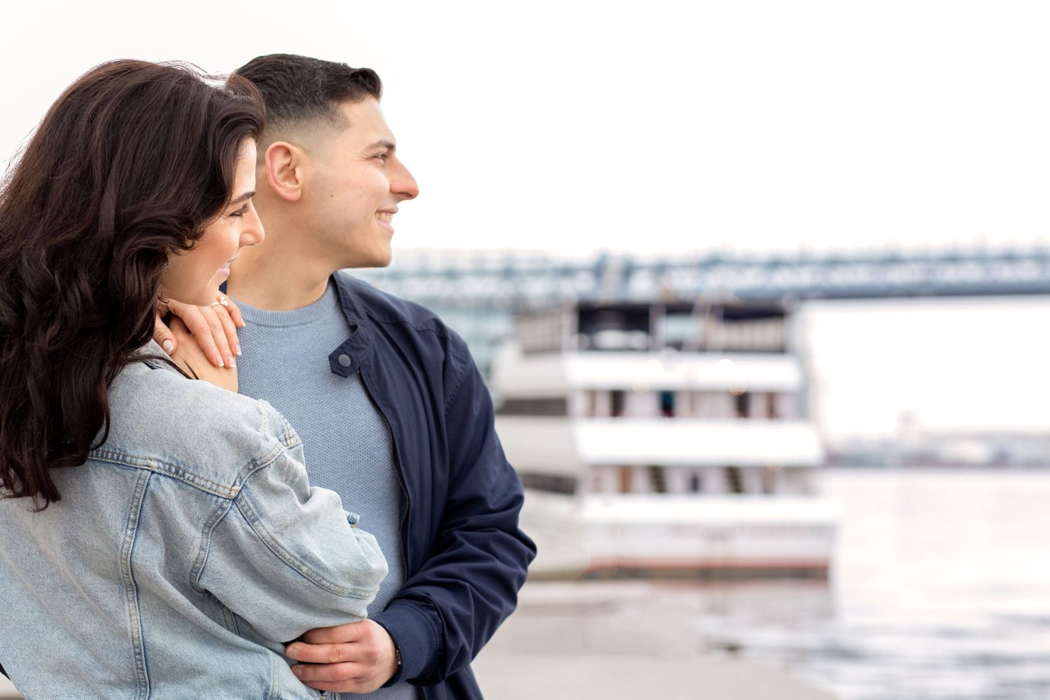 A couple shares tender embraces and smiles in a waterfront setting with boats and docks in the background.