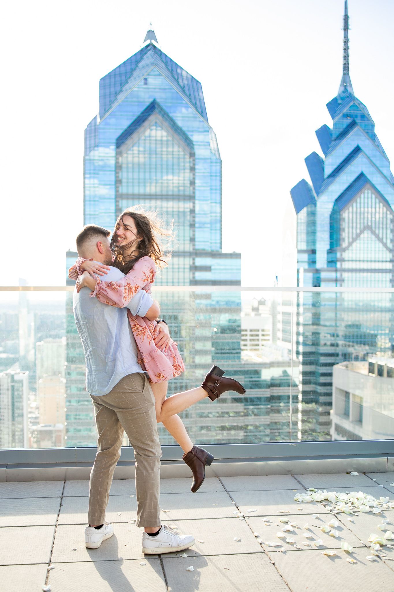 A couple dances and twirls together on a rooftop terrace with Philadelphia's iconic skyscrapers in the background.