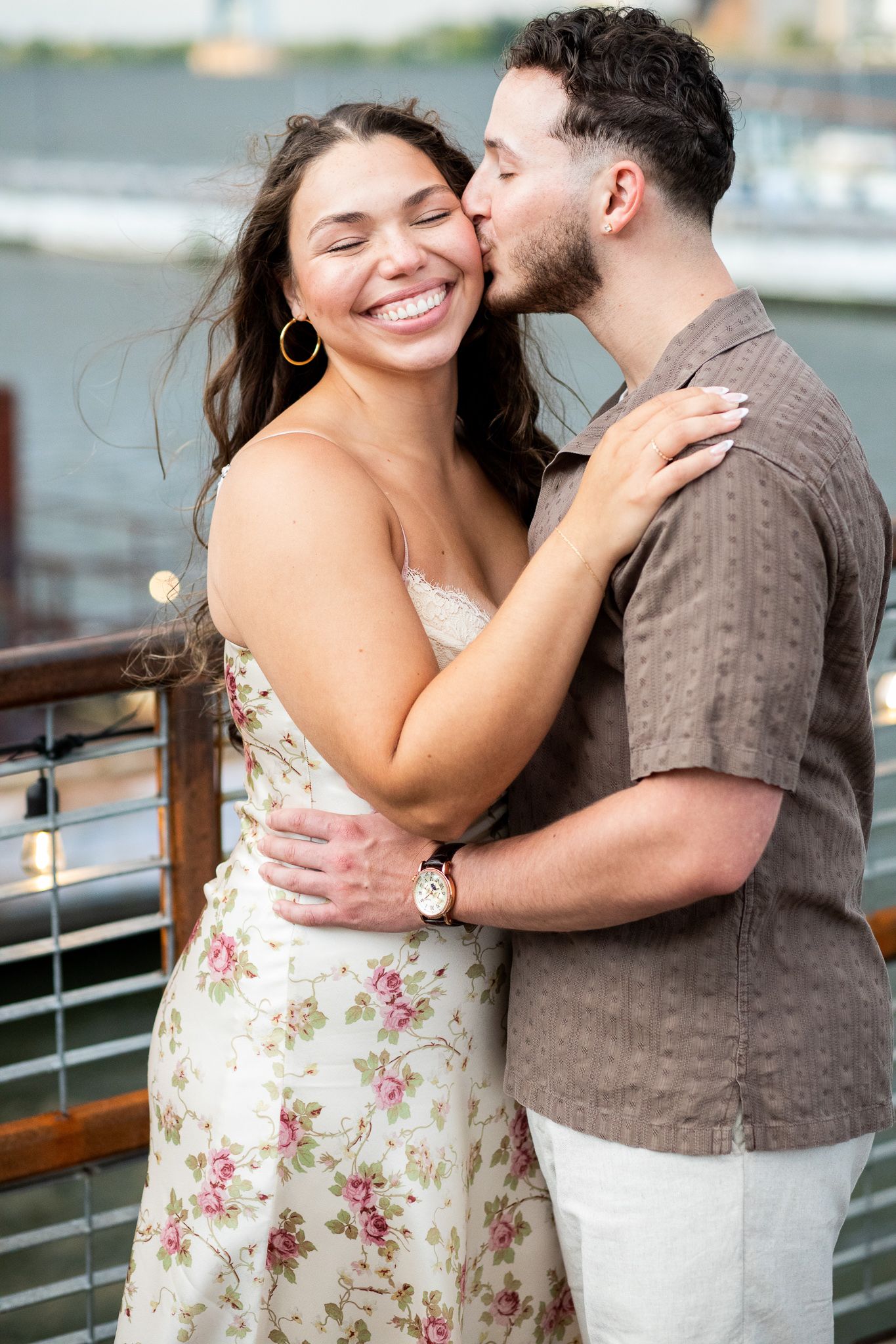 A couple shares intimate moments during their engagement photoshoot on a waterfront deck.