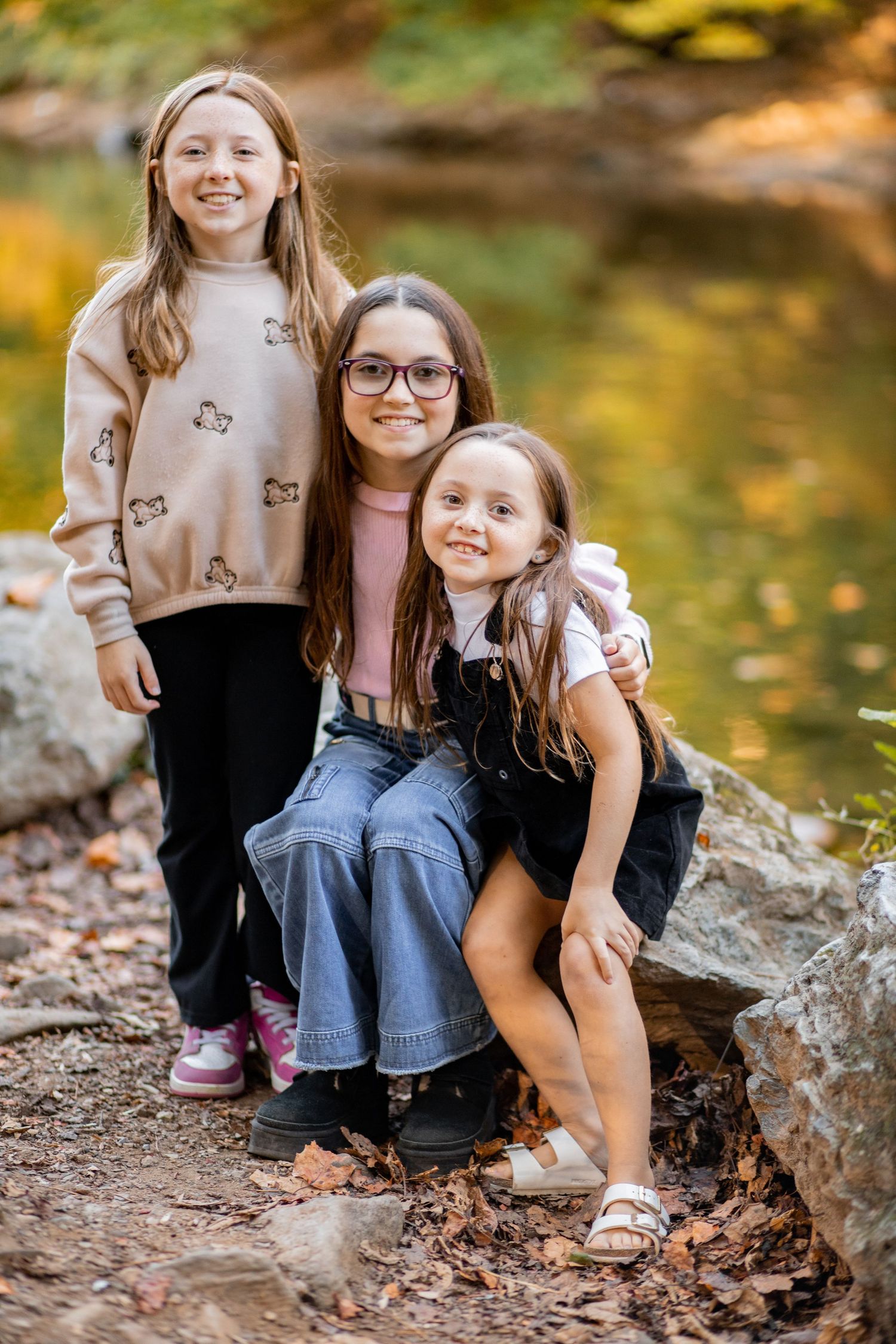 Five heartwarming fall photos of siblings sitting together on rocks surrounded by autumn leaves and golden bokeh.