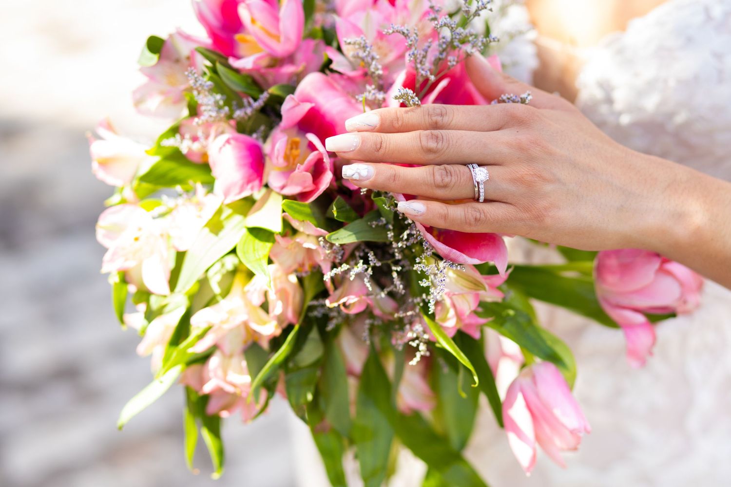 A hand wearing an engagement ring holds a vibrant pink and white bridal bouquet with roses and mixed flowers.