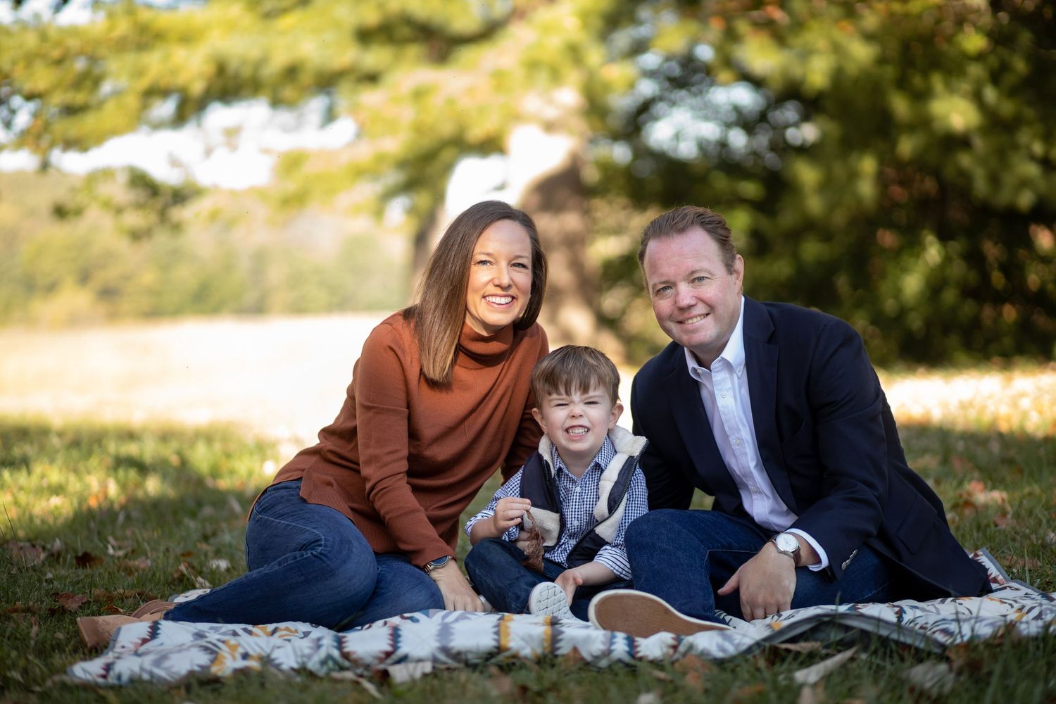 A happy couple laughs while laying on a blanket outdoors during an autumn photoshoot session.