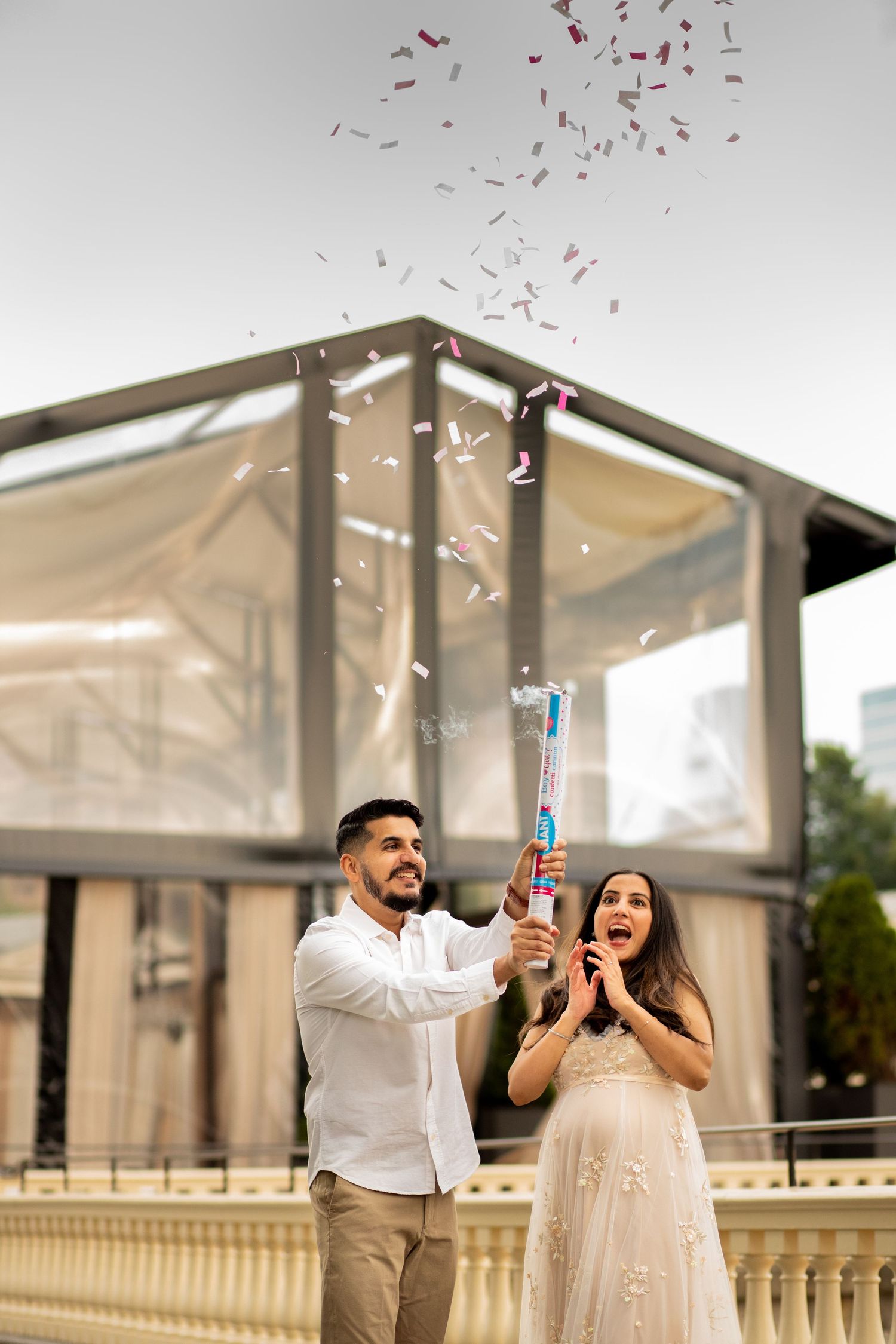 A pair celebrates joyfully with champagne splashing and confetti falling at an elegant outdoor venue during sunset.