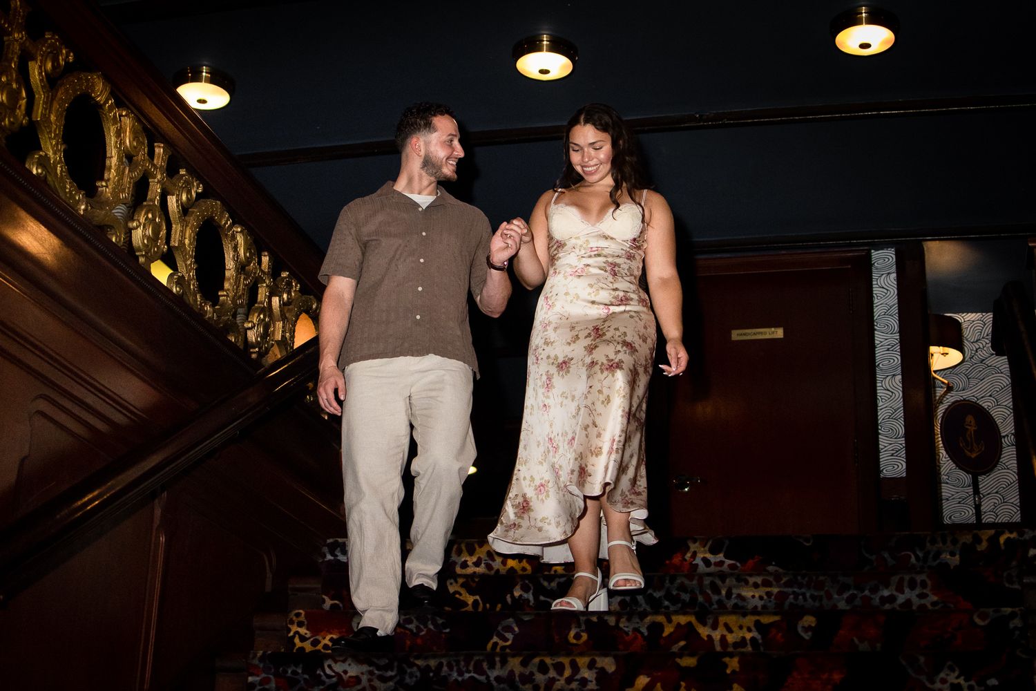 Couple walking down a dimly lit staircase in a restaurant or bar setting.