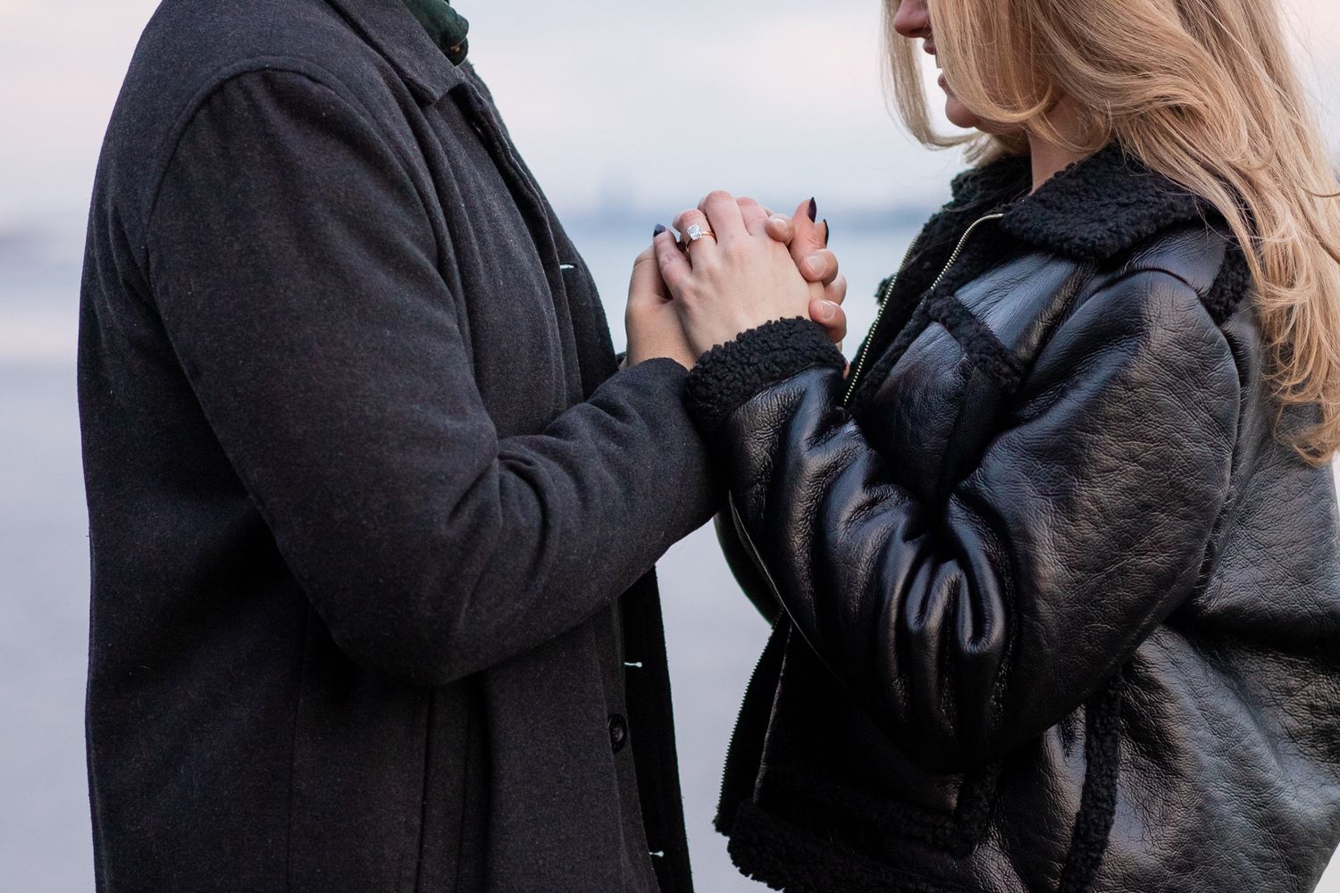 A couple in dark winter coats share a tender moment while walking together on a snowy path.