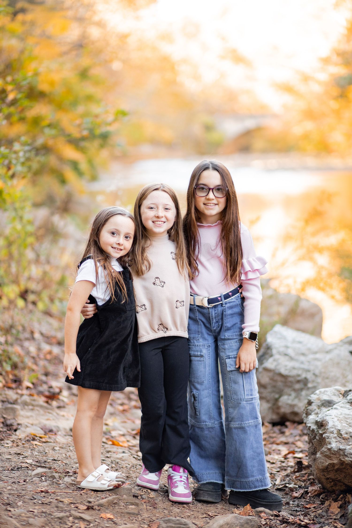 Young friends in casual clothing sit together outdoors amid golden autumn foliage and rocks.