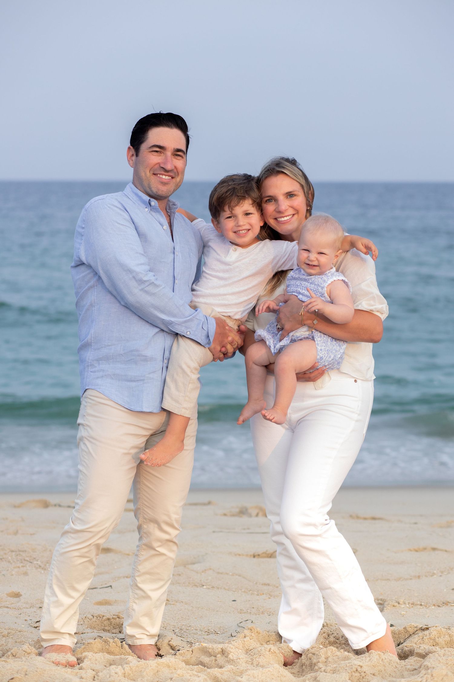 A family creates joyful moments together during a beach photoshoot in matching white and beige outfits near the ocean.