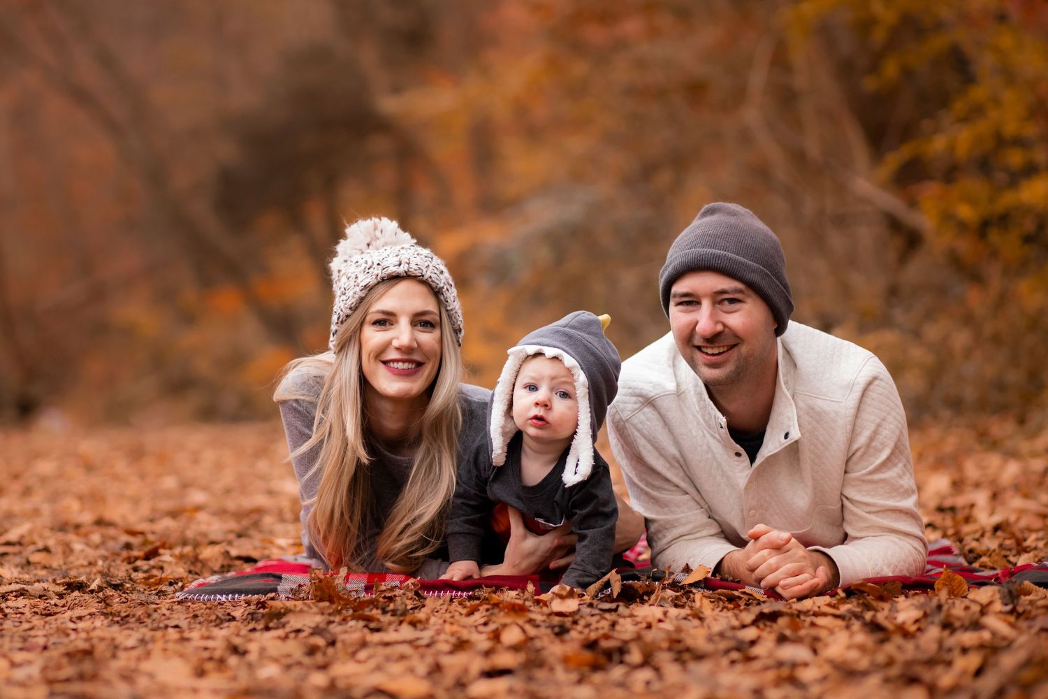 Family enjoying fall foliage while lying in colorful autumn leaves during an outdoor photo session.