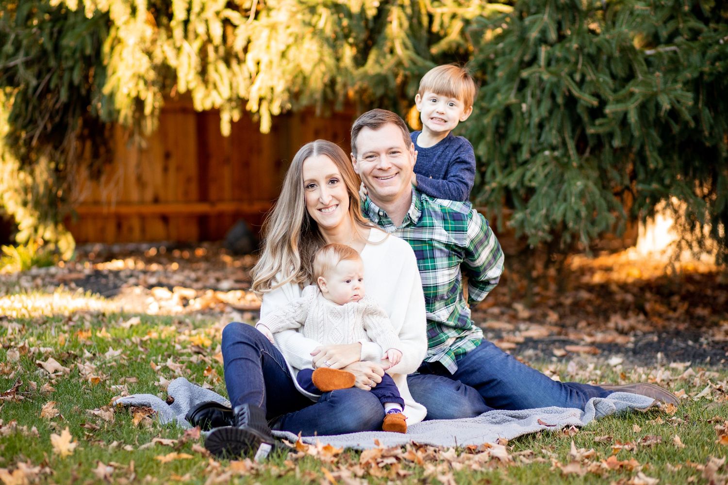 A family sits together on a blanket outdoors in autumn with golden sunlight filtering through trees behind them.