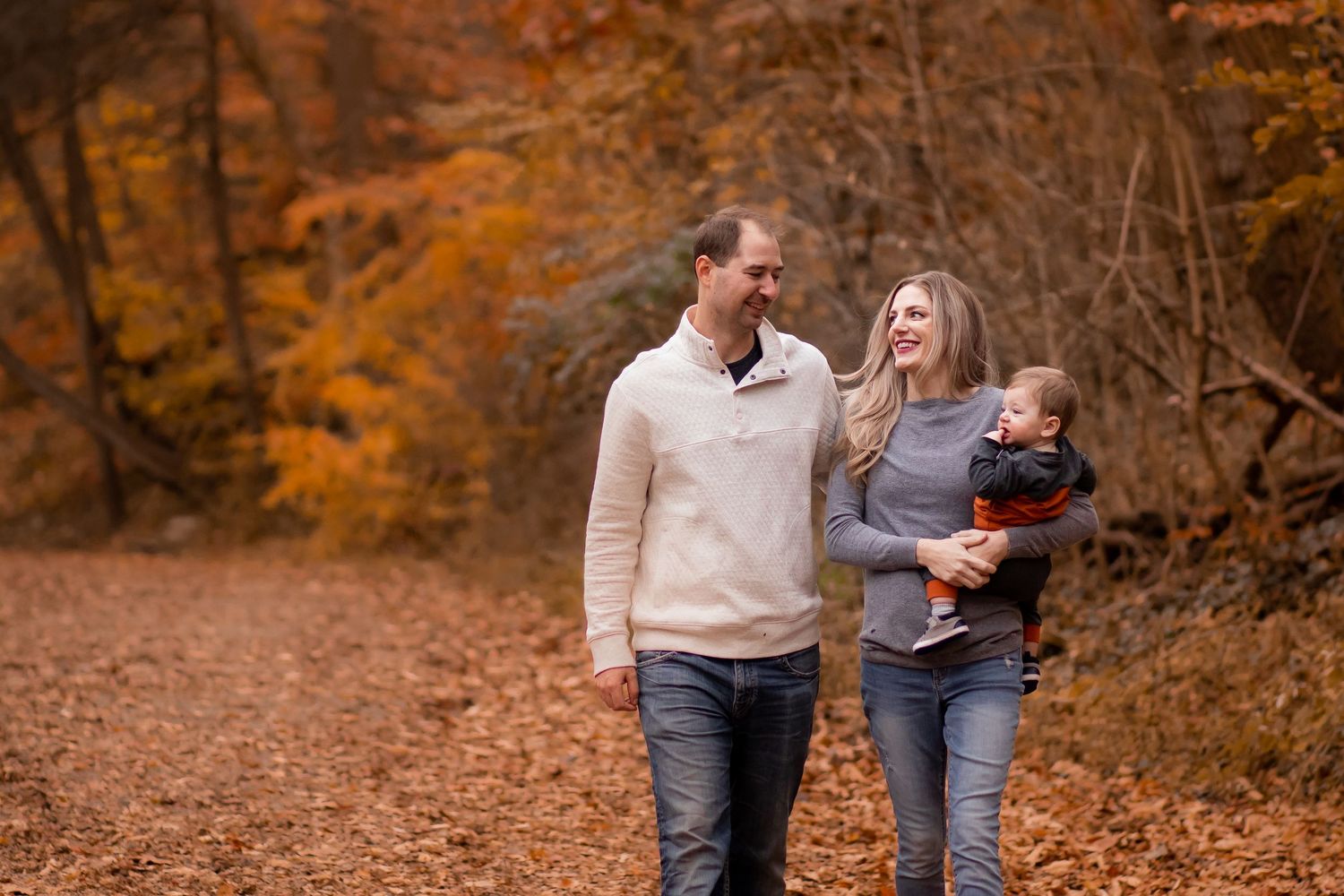 A couple laughs together while walking through vibrant autumn foliage in a forest setting.