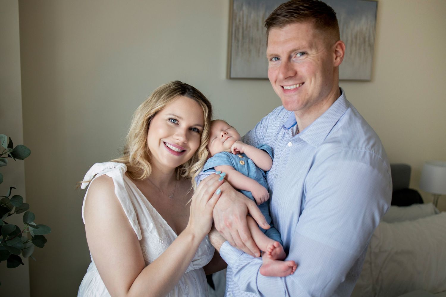 A couple holds their newborn baby together in a cozy indoor setting with soft natural lighting.