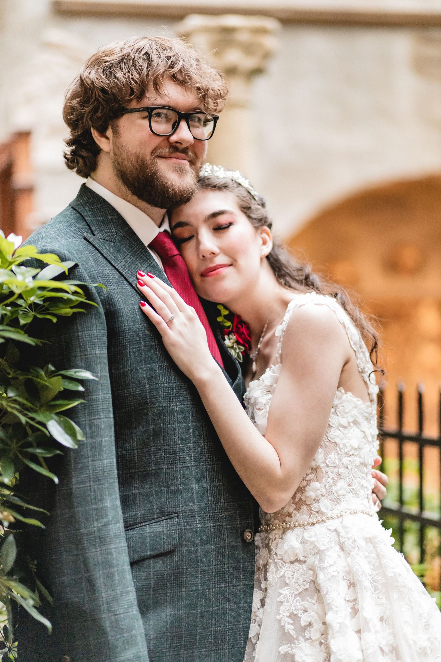 A romantic wedding couple embrace in a garden setting wearing a white lace gown and plaid gray suit.