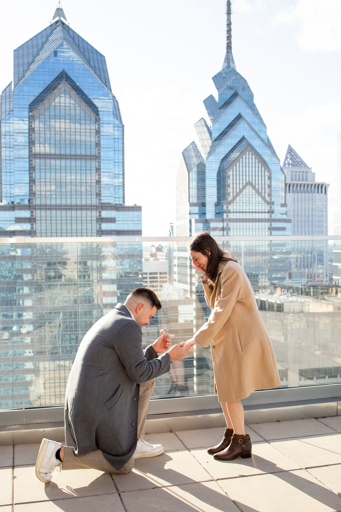 A couple shares a romantic moment on a rooftop observation deck with Philadelphia's iconic Liberty Place towers in view.